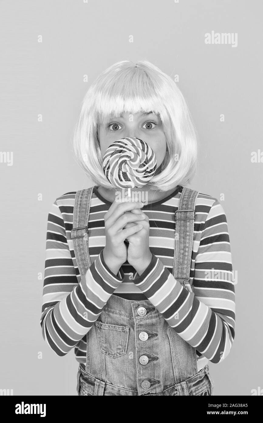 Sweet tooth. Little child hold lollipop candy yellow background. Small girl with rainbow swirl candy on stick. Adorable kid enjoy sugar candy dessert. Best candy shop. Stock Photo