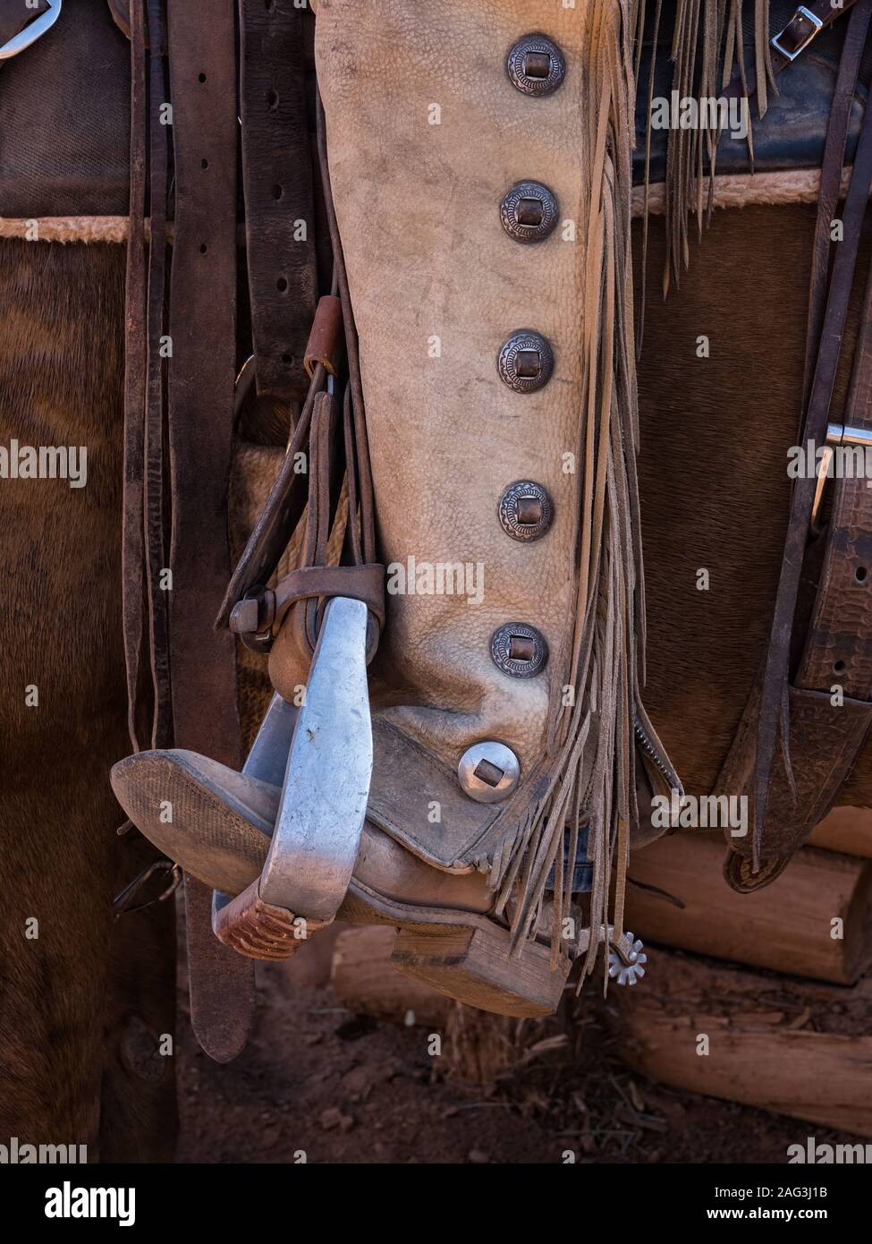 Close up detail of a cowboy's boot in a saddle stirrup with leather chaps and fringe.  The leather chaps protect the cowboy's legs from thorny brush o Stock Photo