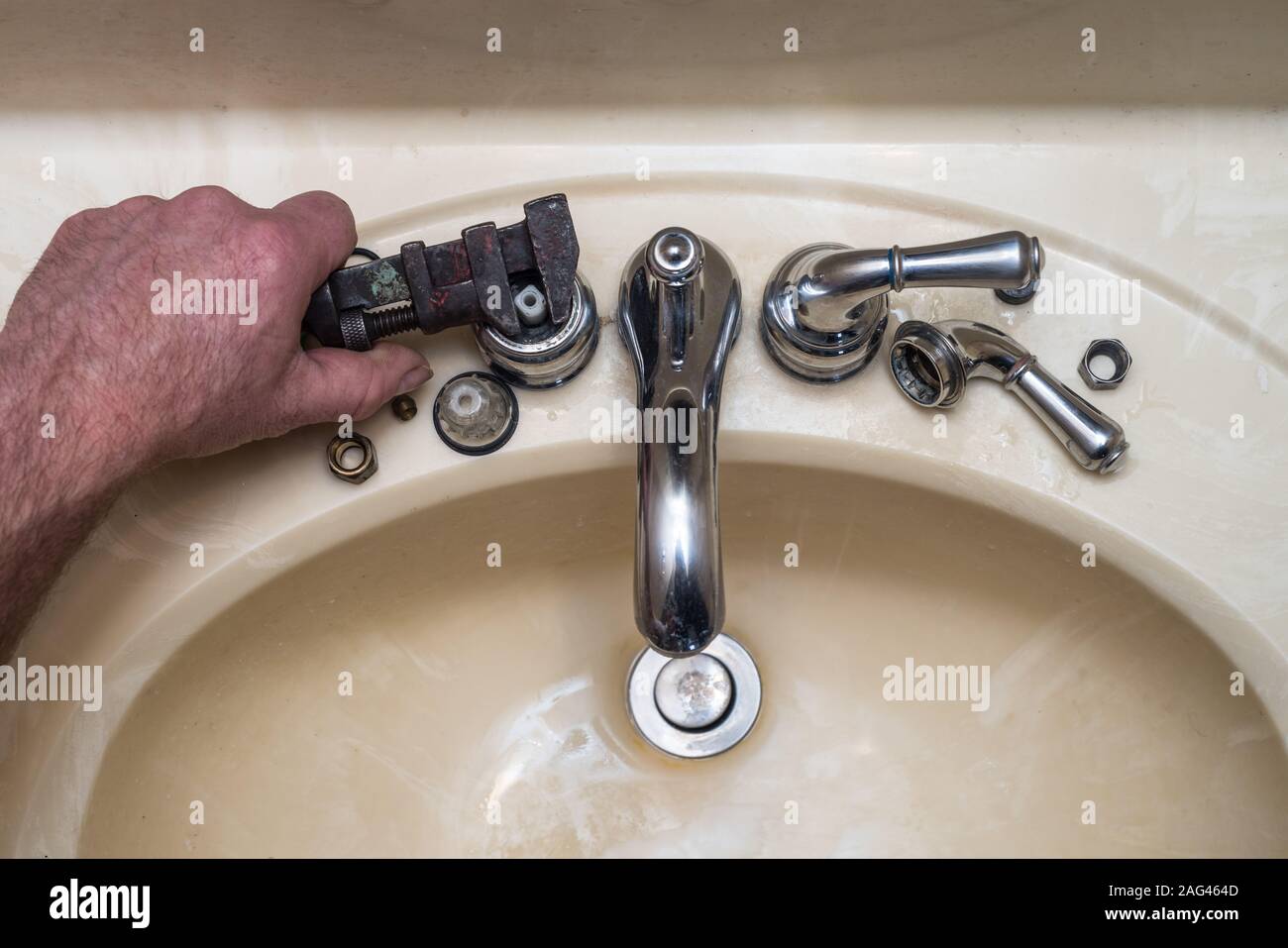 A photo looking down on a broken faucet with a man working to fix it