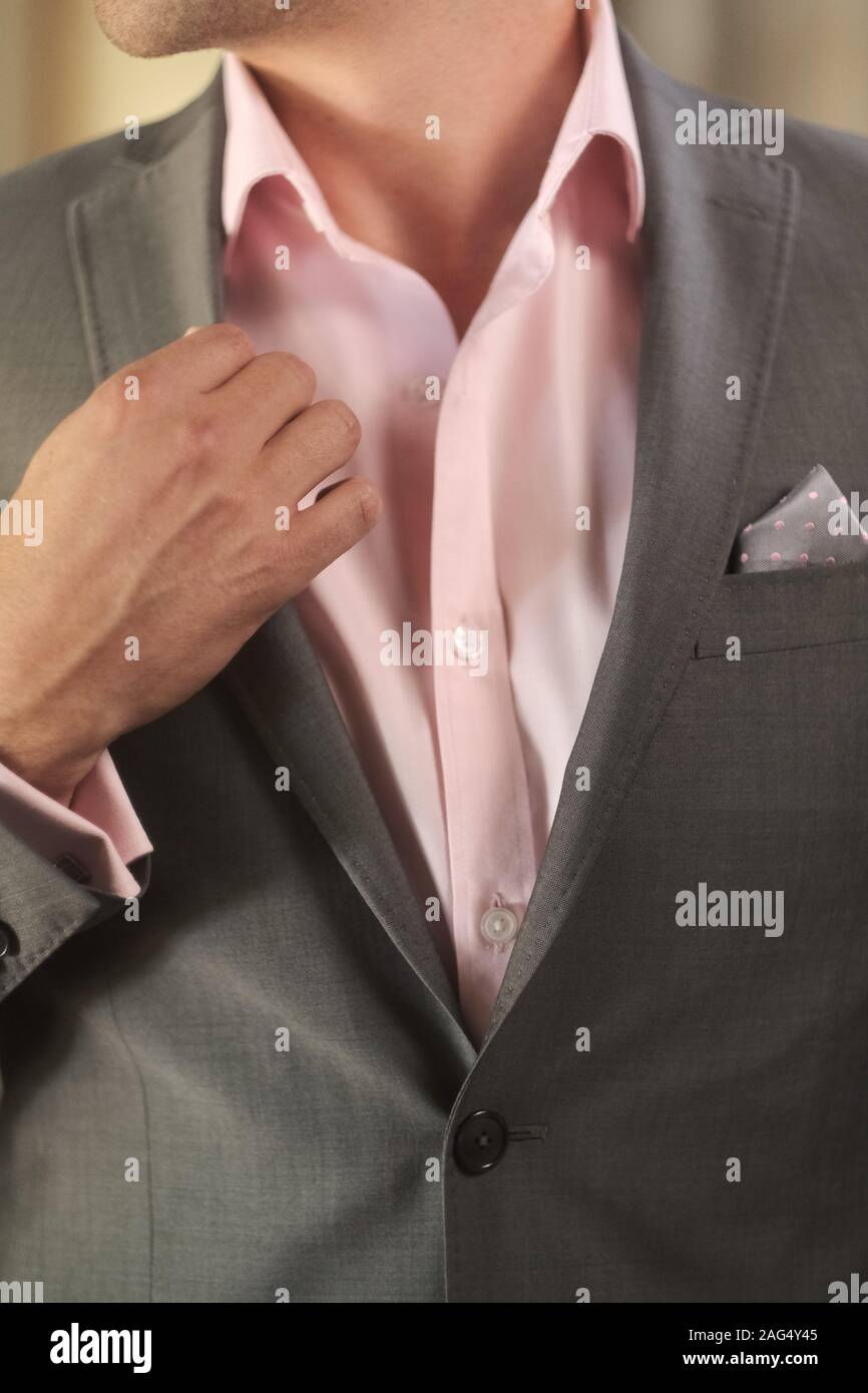 Vertical closeup shot of a groom wearing a pink shirt and grey suit,  getting ready for the wedding Stock Photo - Alamy