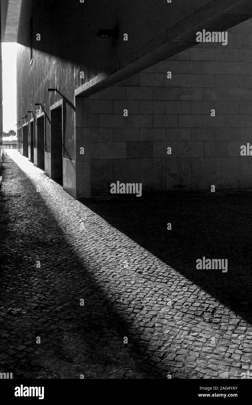 Vertical grey scale shot of the sun shining on the sidewalk through the buildings Stock Photo
