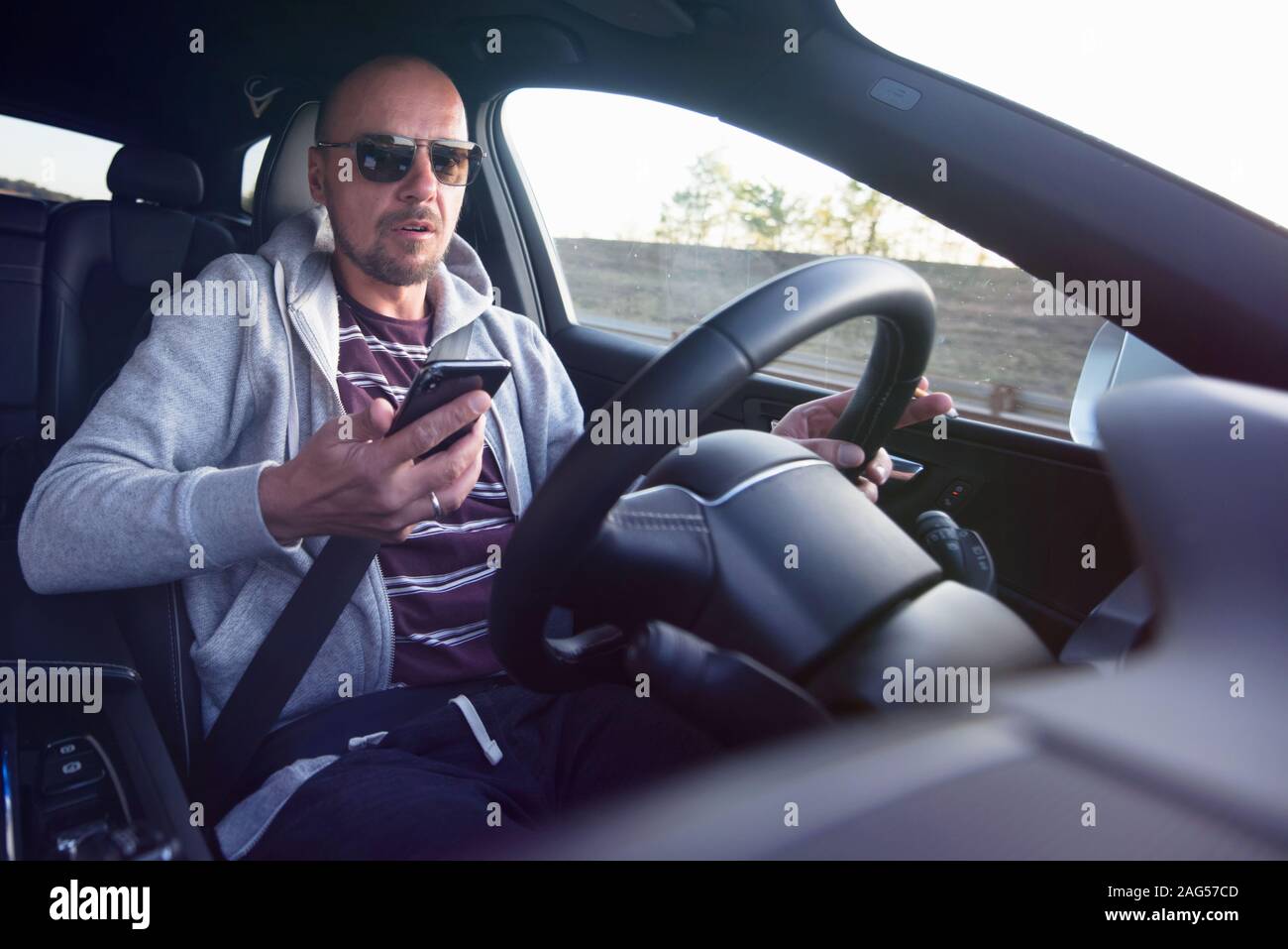 Man looking at mobile phone while driving a car. Stock Photo