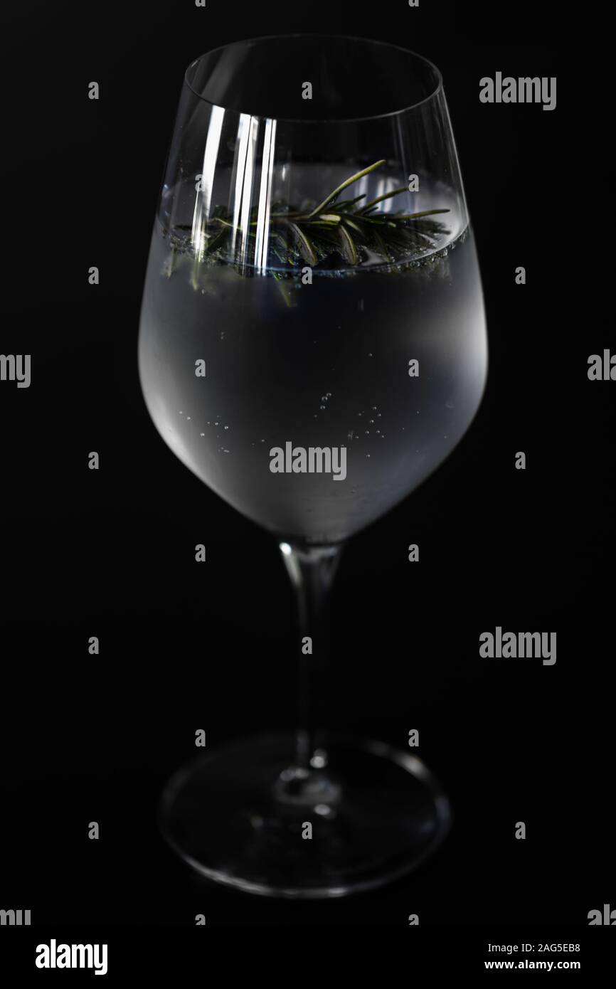 Closeup of a Wine glass with ice cold Gin Tonic with a twig of rosemary for the flavor, isolated before a black background. Stock Photo