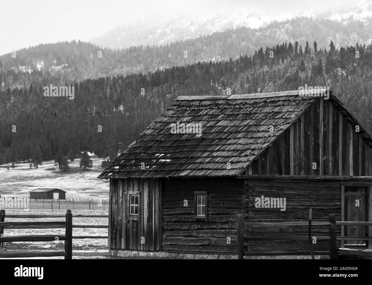 Gray scale shot of a wooden cottage on a farm with the tree covered hills in the background Stock Photo