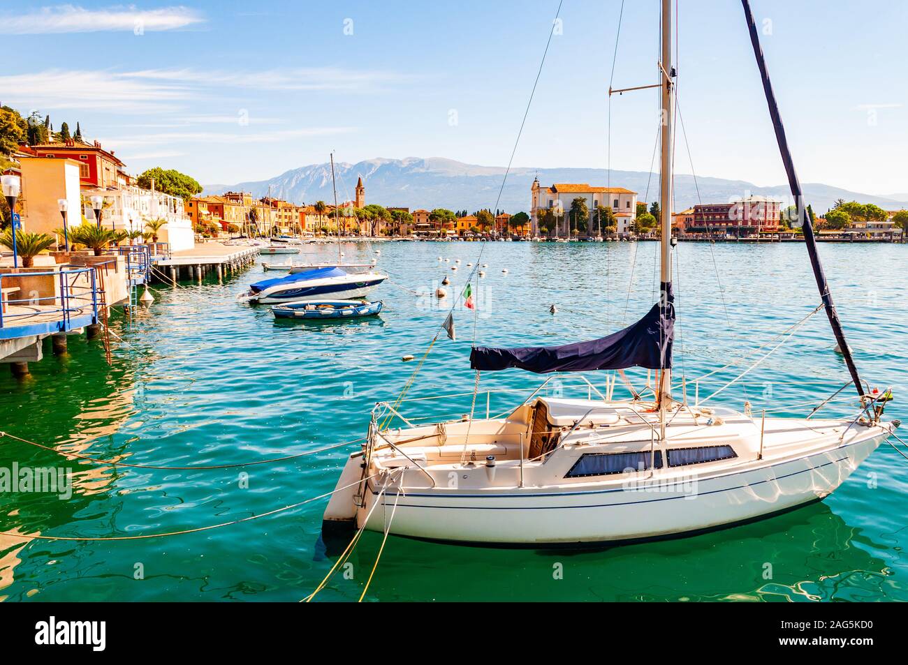 Toscolano Maderno, Lombardy, Italy - September 12, 2019: View on sailing yacht and boats parked on crystal clear blue water of amazing lake Garda and Stock Photo