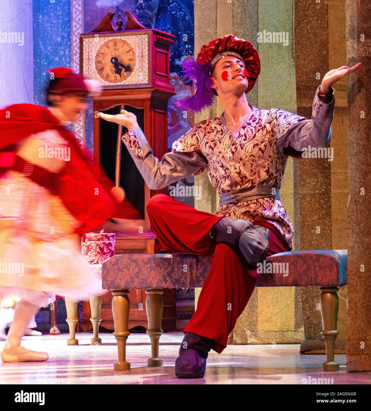 Dancing Boy Doll dancer poses in costume as another dancer rushes past in a blur of color before the start of the dress rehearsal of The Nutcracker. Stock Photo