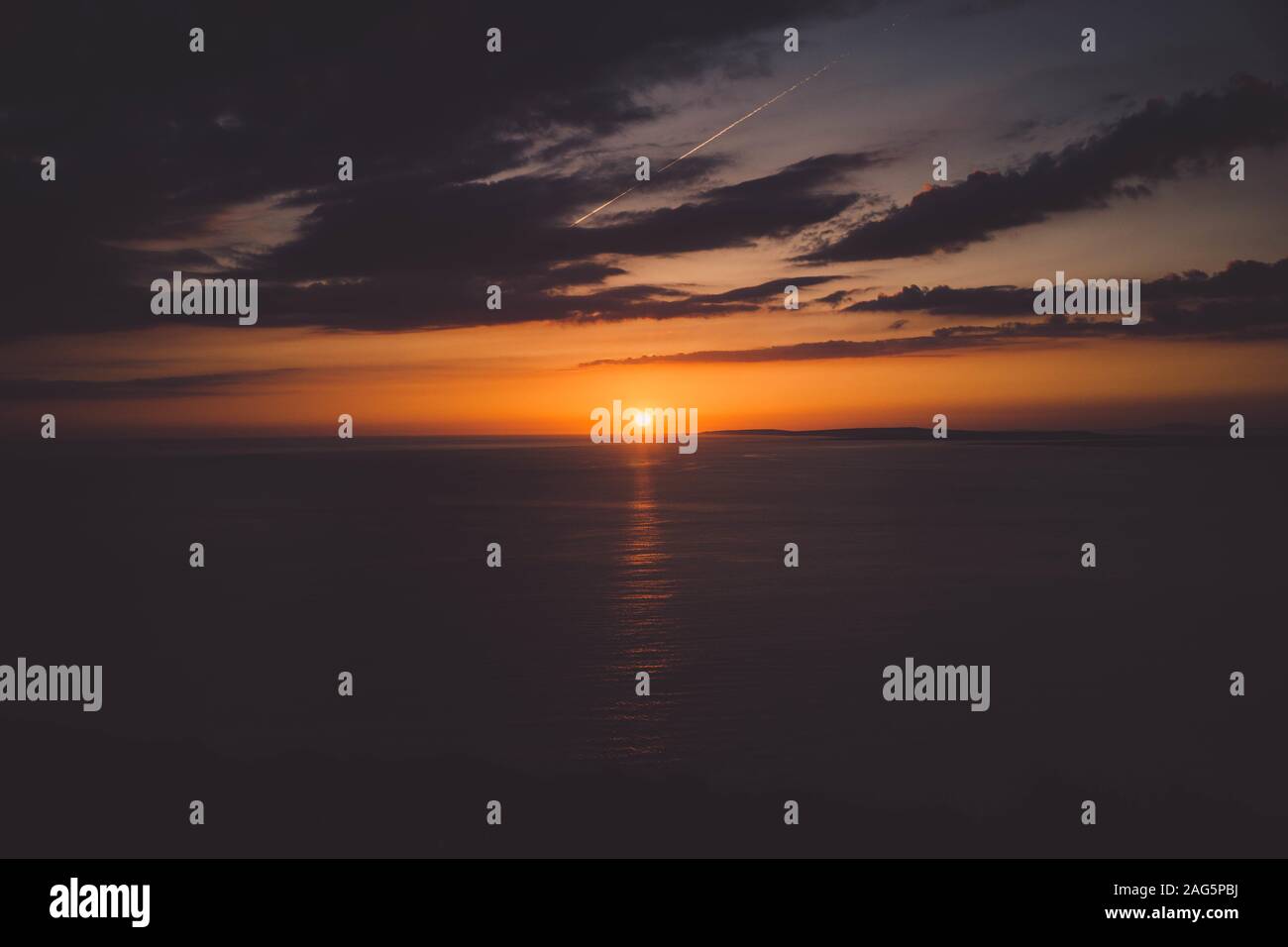 Breathtaking view of the sunset over the horizon of a beautiful calm ocean under the cloudy sky Stock Photo