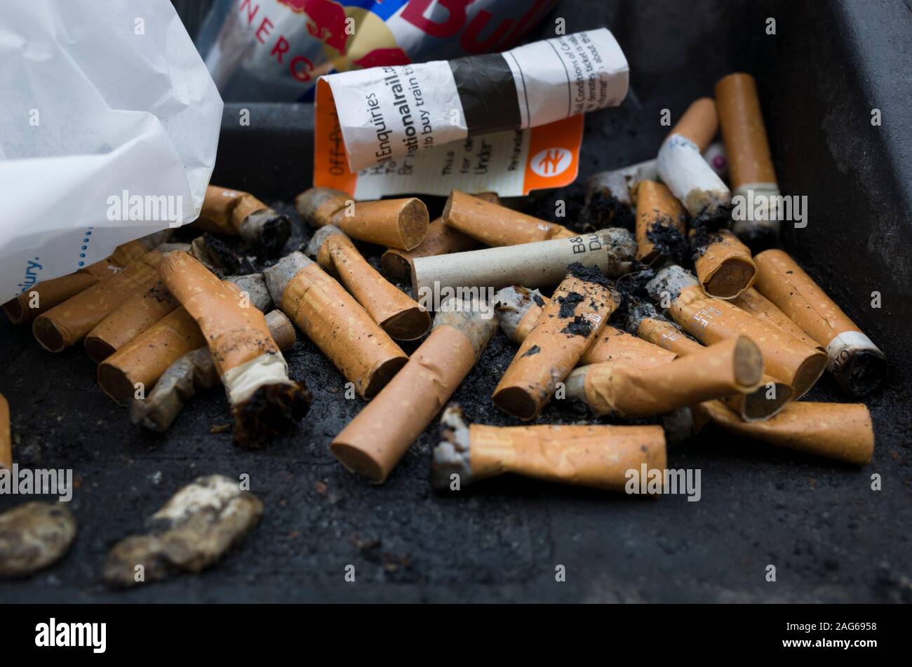 Discarded burnt cigarettes and litter on rubbish bin lid Stock Photo