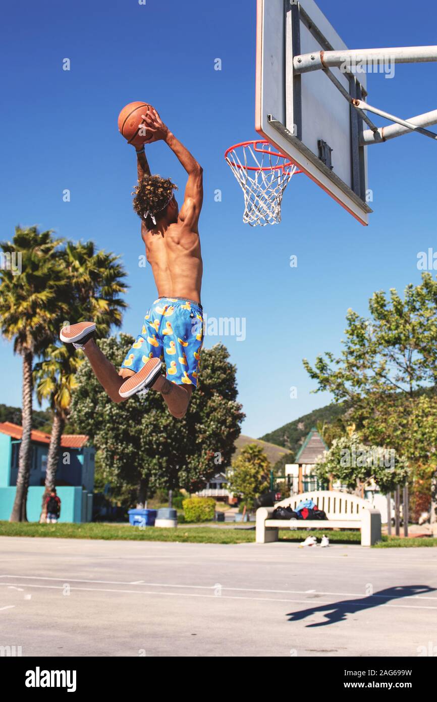 Male with blue and yellow shorts making a dunk in the basketball court during daytime Stock Photo