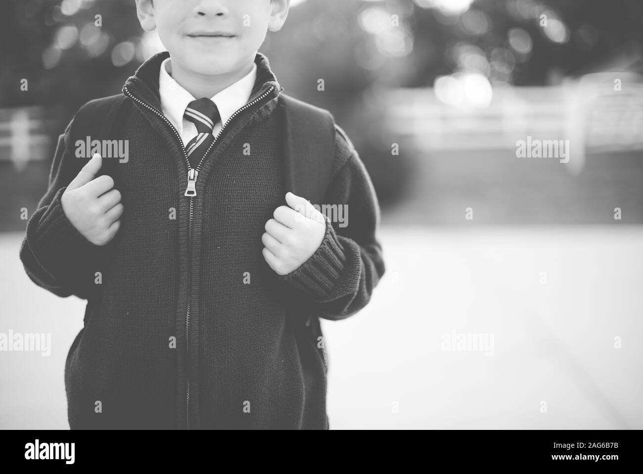 Grayscale shot of a child wearing a school uniform and a backpack with a blurred background Stock Photo