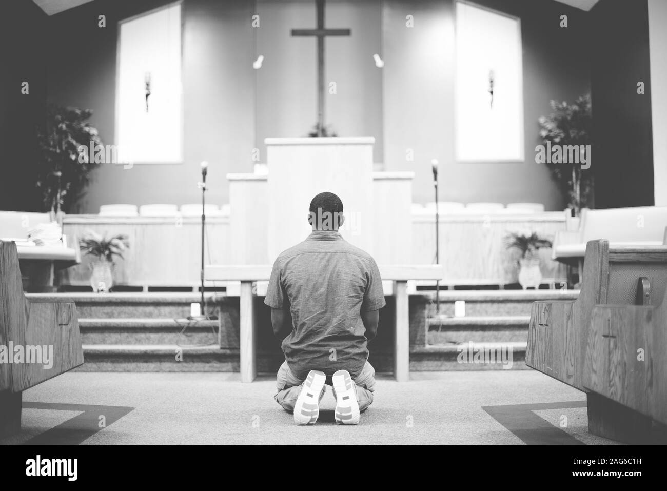Grayscale of a male on his knees praying in the church with a blurred  background Stock Photo - Alamy