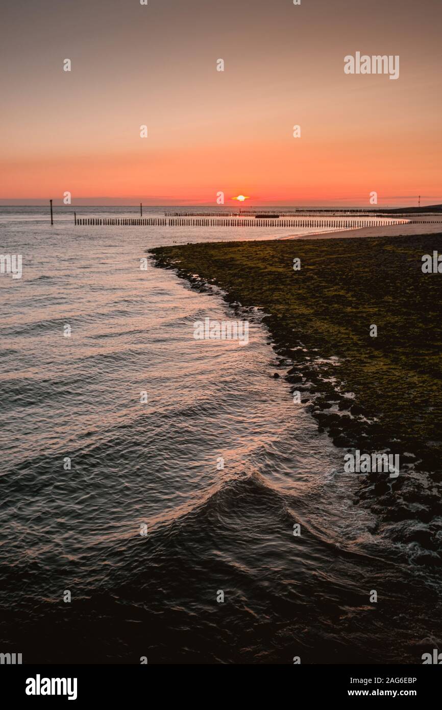 Vertical shot of the sea and the beach with a beautiful sunset in the sky in the background Stock Photo