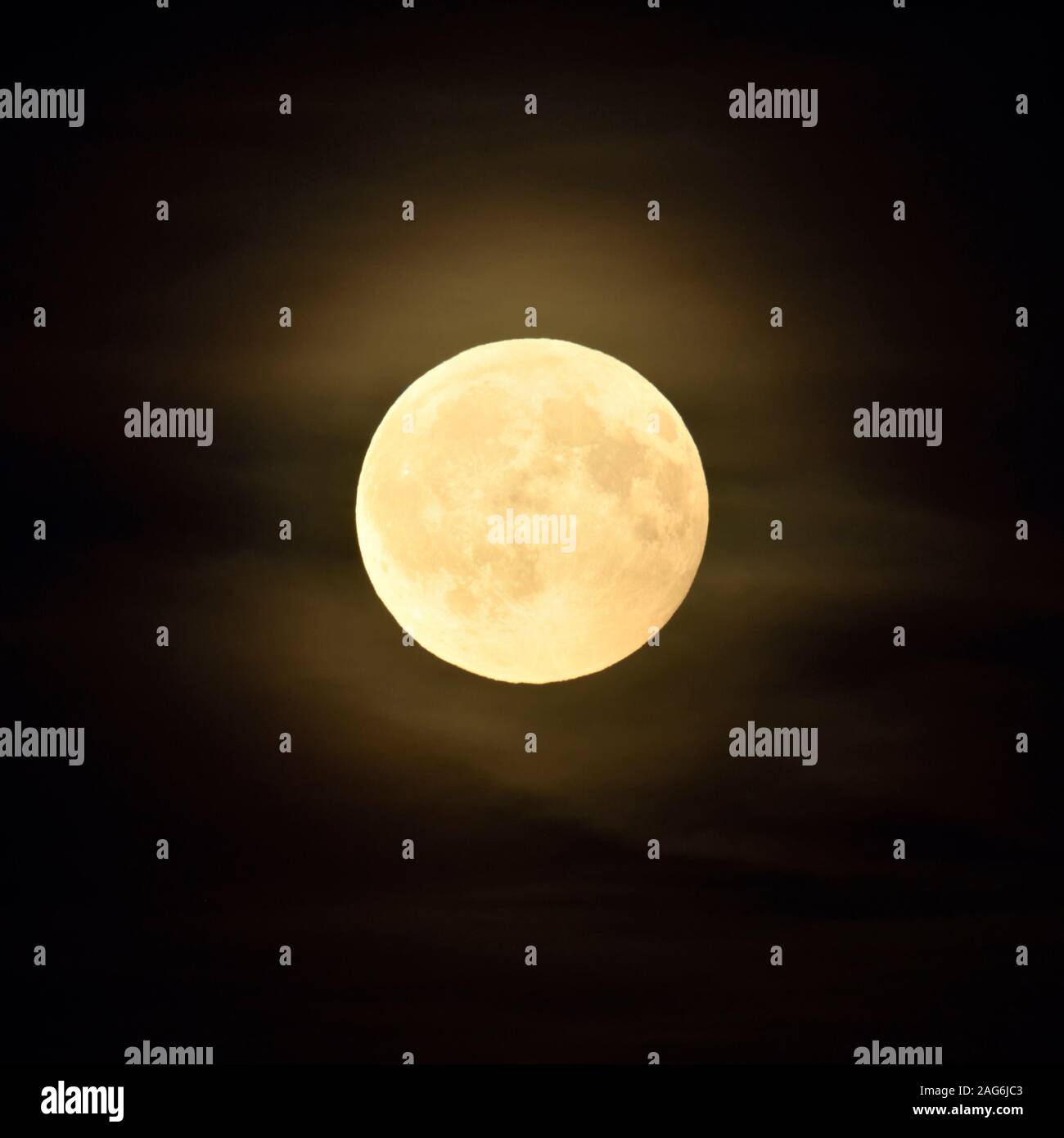 Full moon / Vollmond shining bright in dark night, amber moon with some few puffy, hazy clouds. Stock Photo