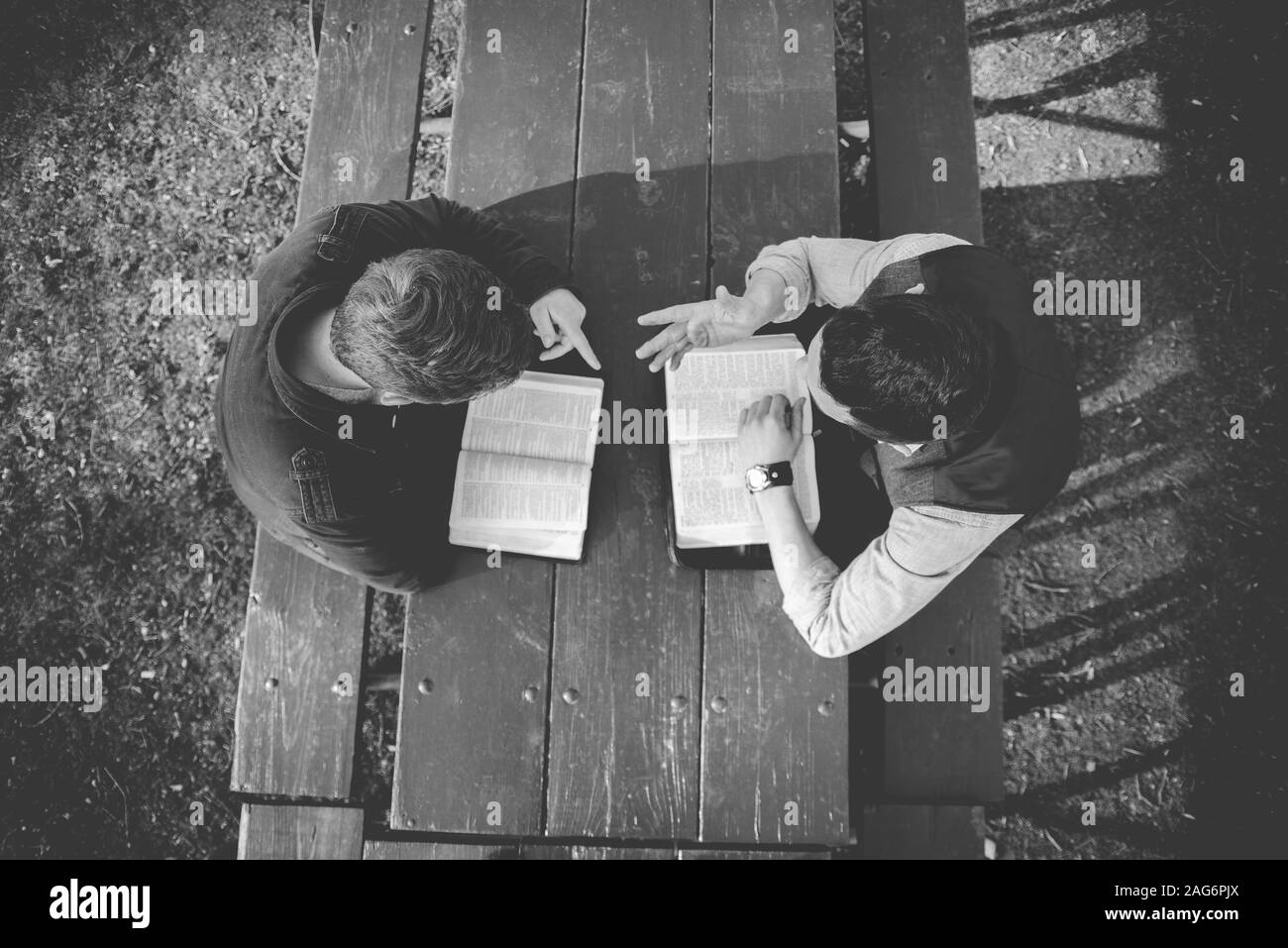 Overhead shot of two males sitting in the park and reading the bible in black and white Stock Photo