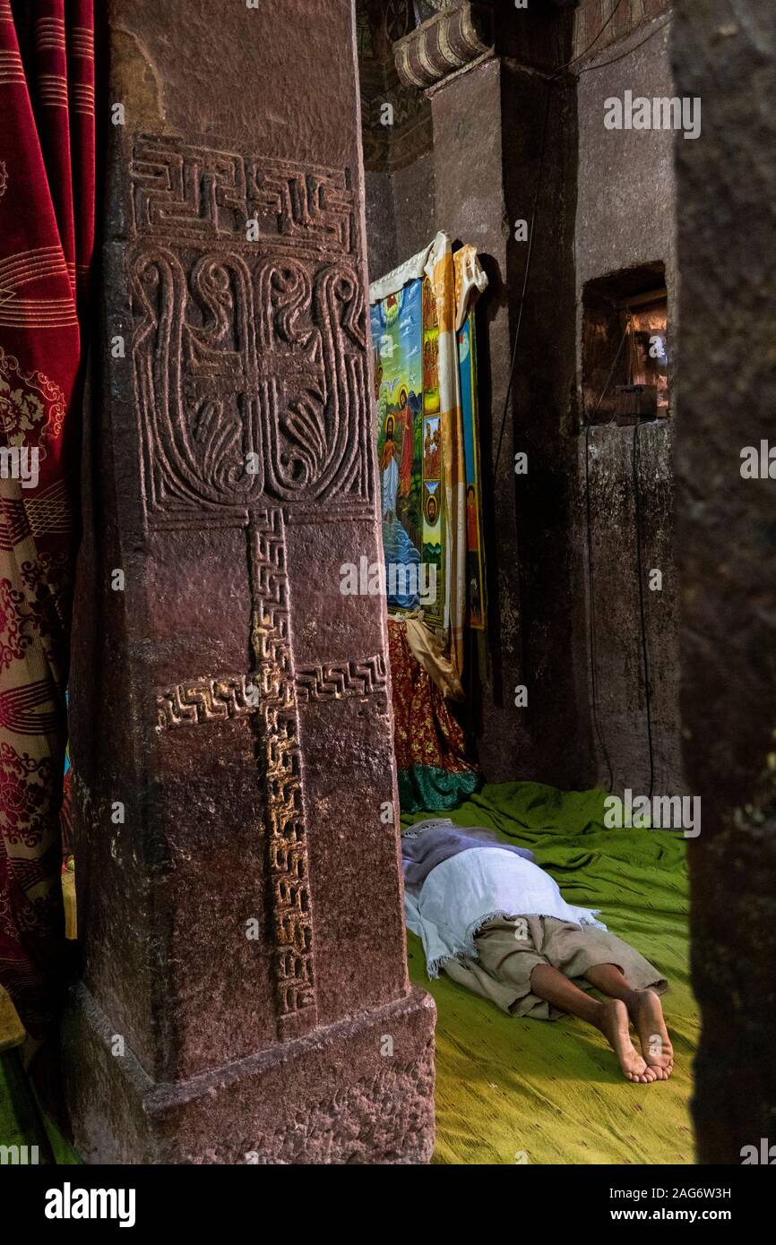 Ethiopia, Amhara Region, Lalibela, inside Bet Maryam Church, devotee prostrating in prayer beyond stone pillar with cruciform carved painted design Stock Photo
