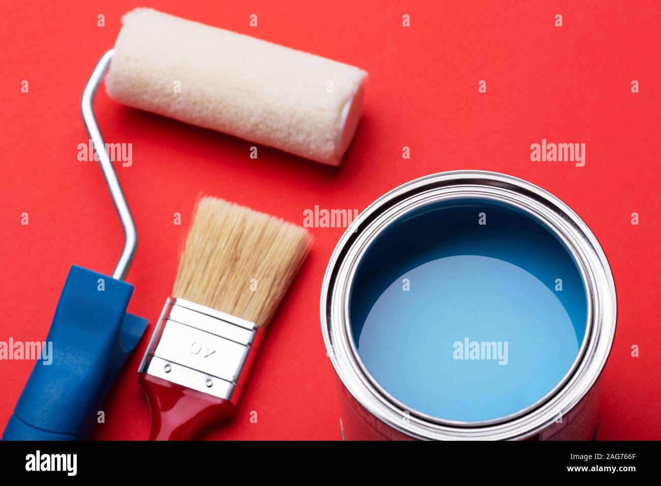 Can of blue paint with brushe and paint roller on red background. Close up view. Repair concept. Stock Photo
