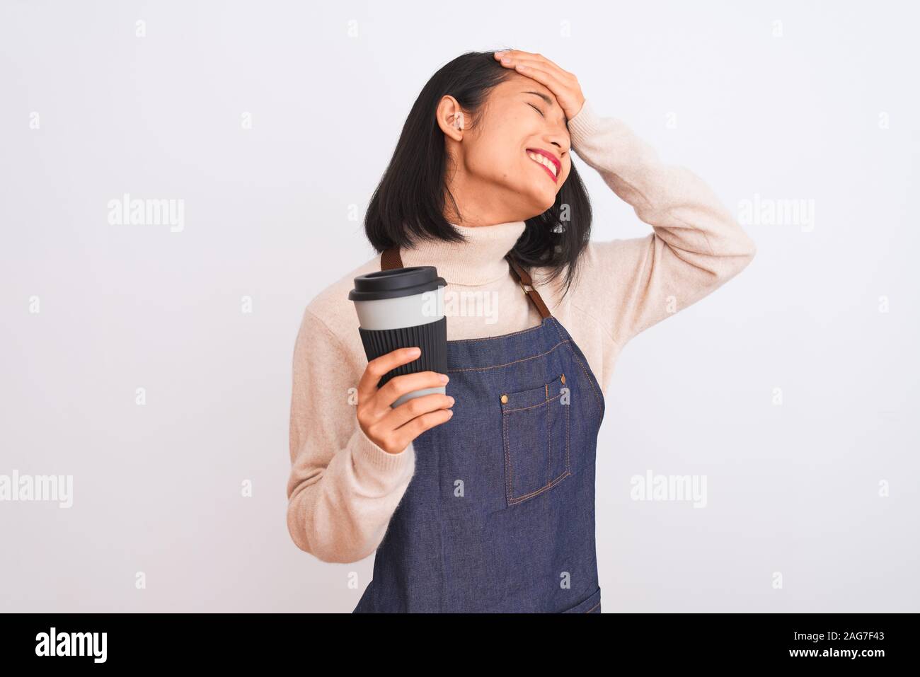 Beautiful barista chinese woman wearing apron holding coffee over isolated white background stressed with hand on head, shocked with shame and surpris Stock Photo