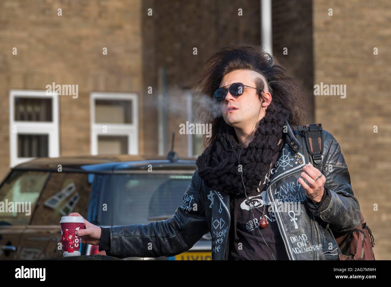 A leather jacketed man wih big hair enjoys a cigarette and a coffee. Stock Photo