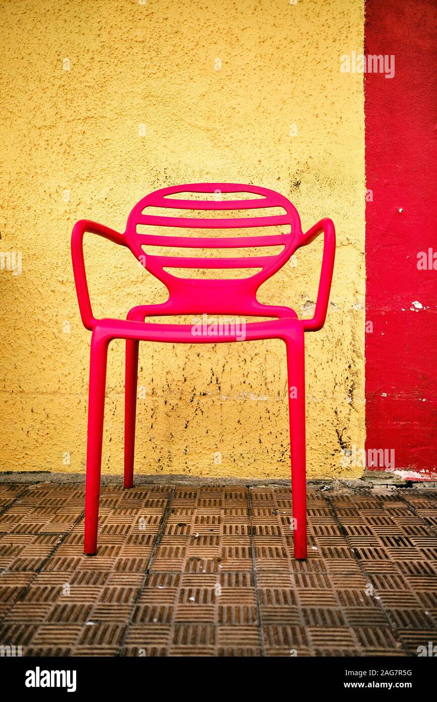 A Vertical Shot Of A Red Chair In Front Of A Yellow And Red Wall
