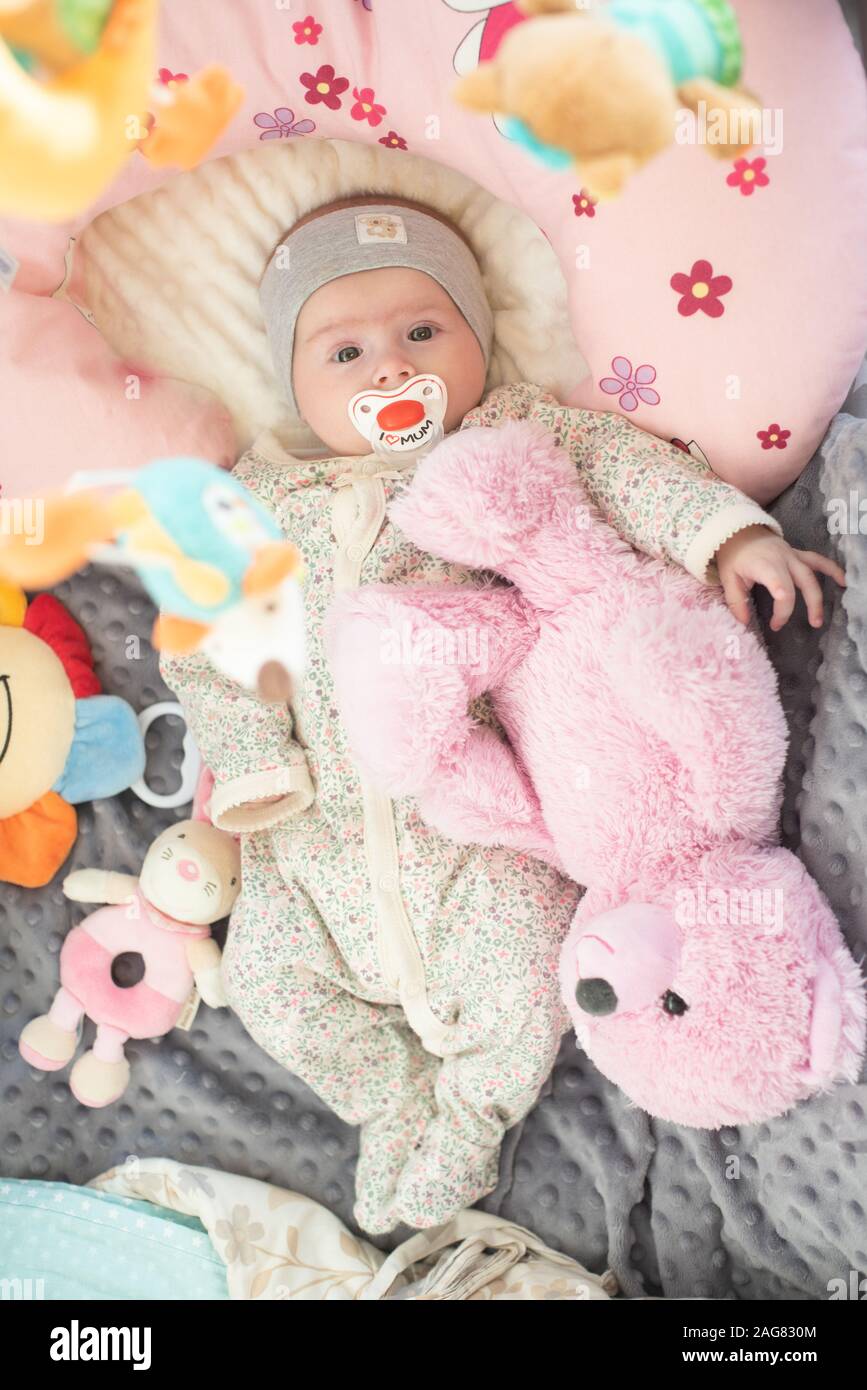 Happy Baby Girl Lying In His Crib With Soother And Pink Bear Stock