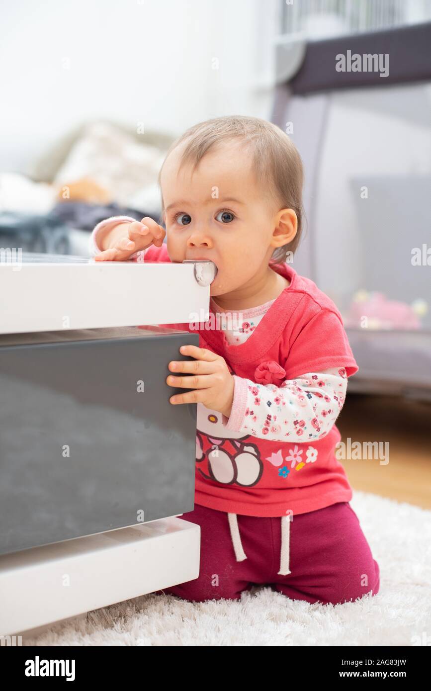 Cute caucasian 1 year old baby girl bites silicon corner protector, concept of teething, Child bites furniture Stock Photo
