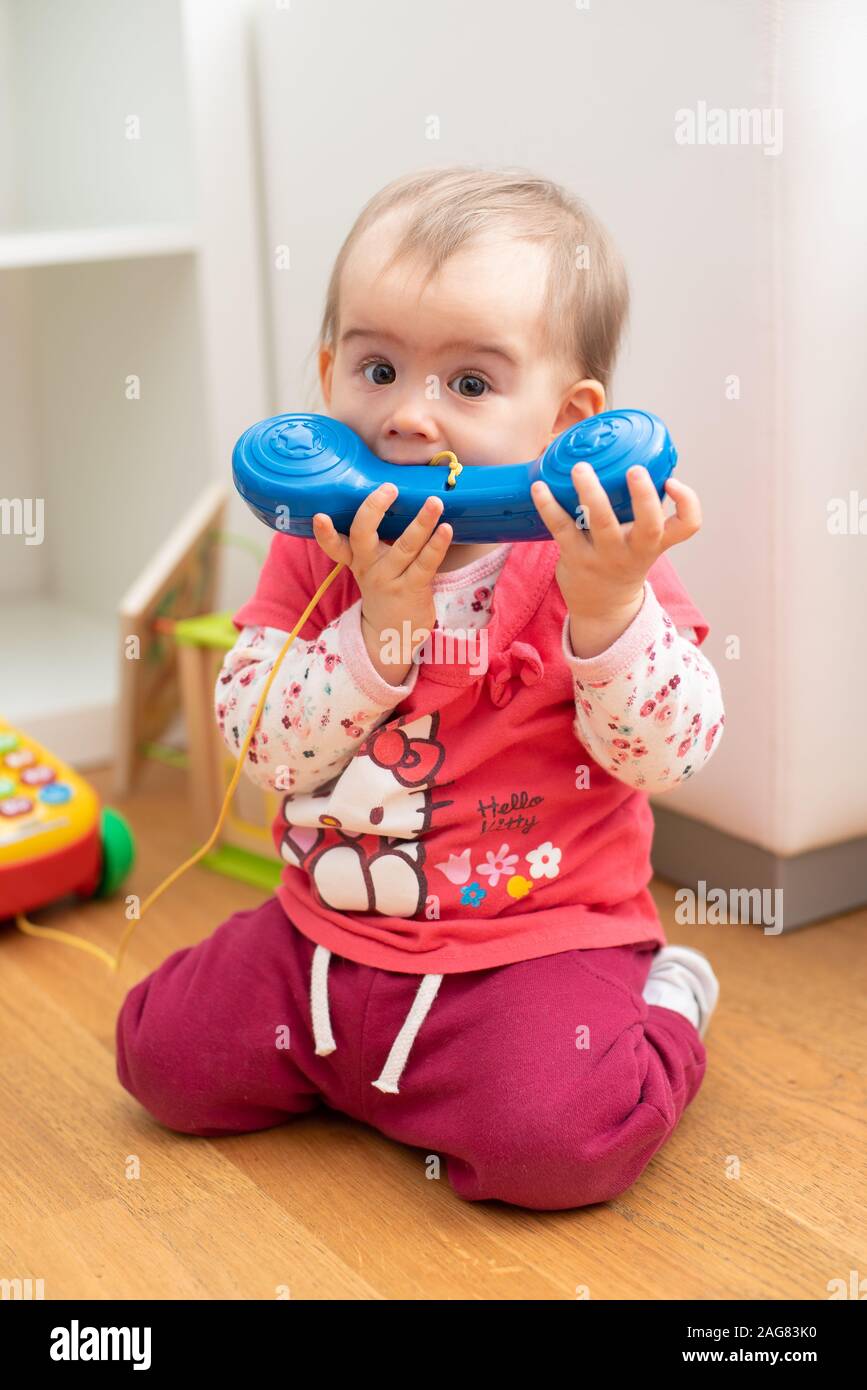 Cute caucasian 1 year old baby girl bites blue phone toy, concept of