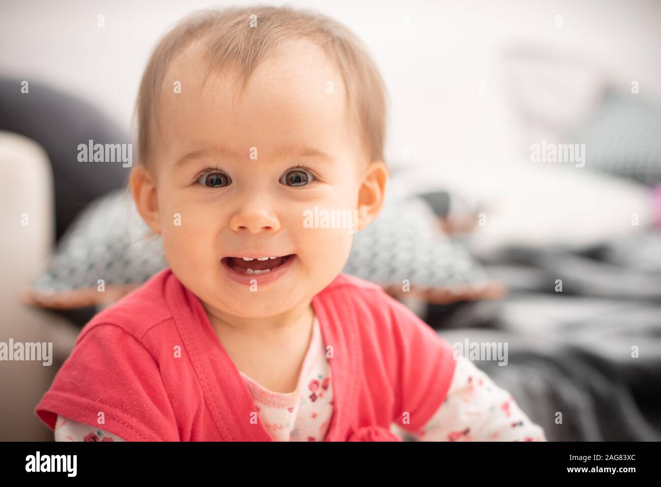 Cute 1 year old baby girl laughs into camera big brown eyes and wide smile with new teethes, concept of teething. Stock Photo