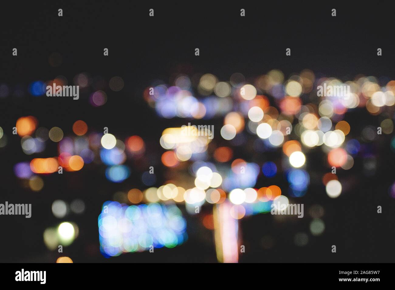 Blurred shot of city buildings with lit lights at night time Stock Photo