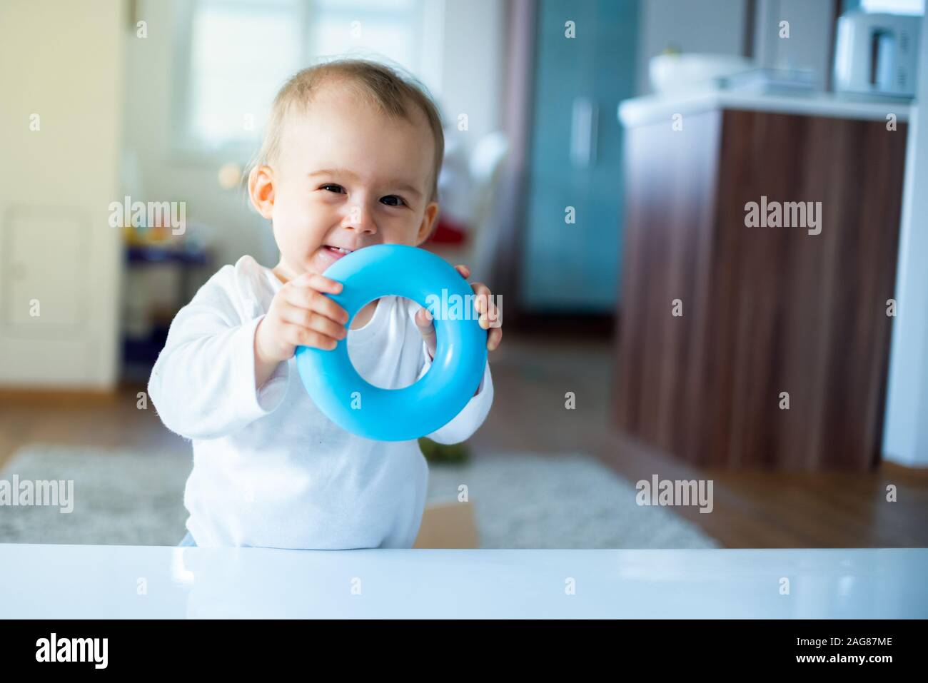 Caucasian baby girl standing next to table with blue torus in hands and laughing Stock Photo
