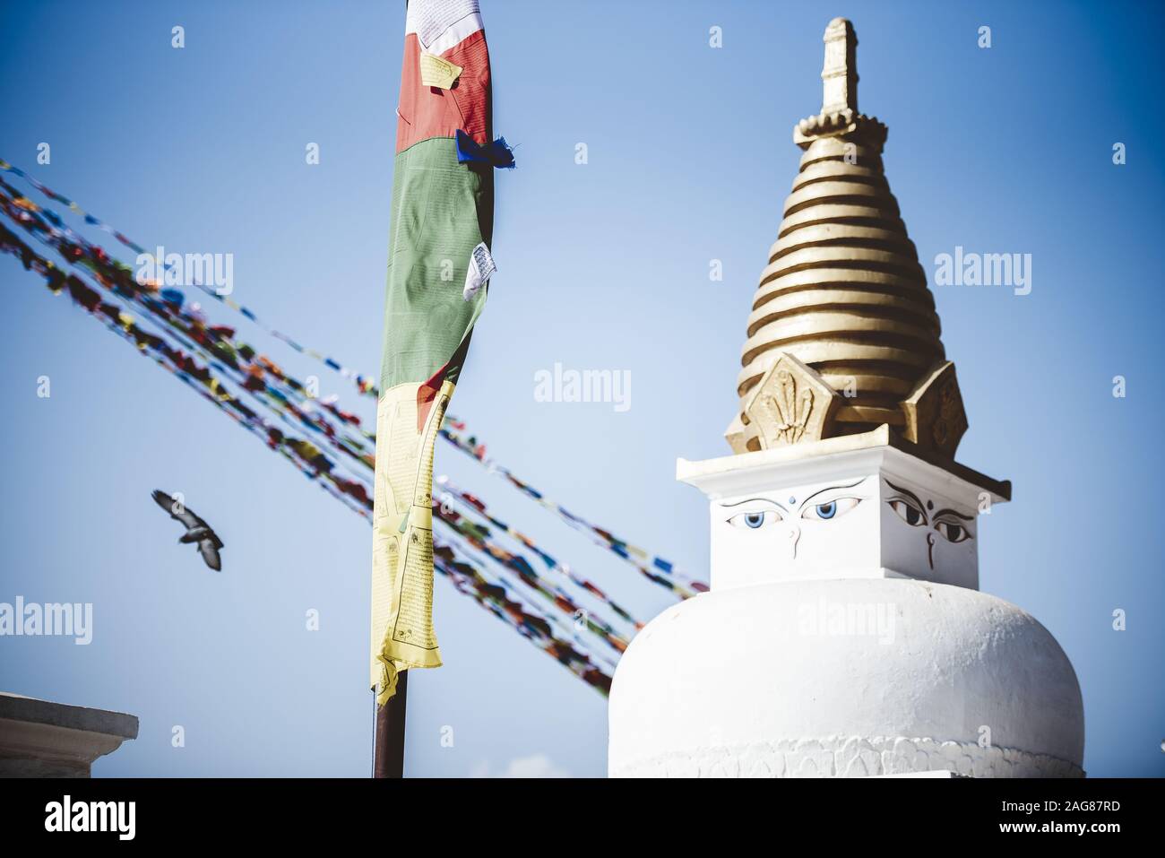 Closeup shot of a pole with prayer cloths wrapped around it near a temple with eyes painted on it Stock Photo