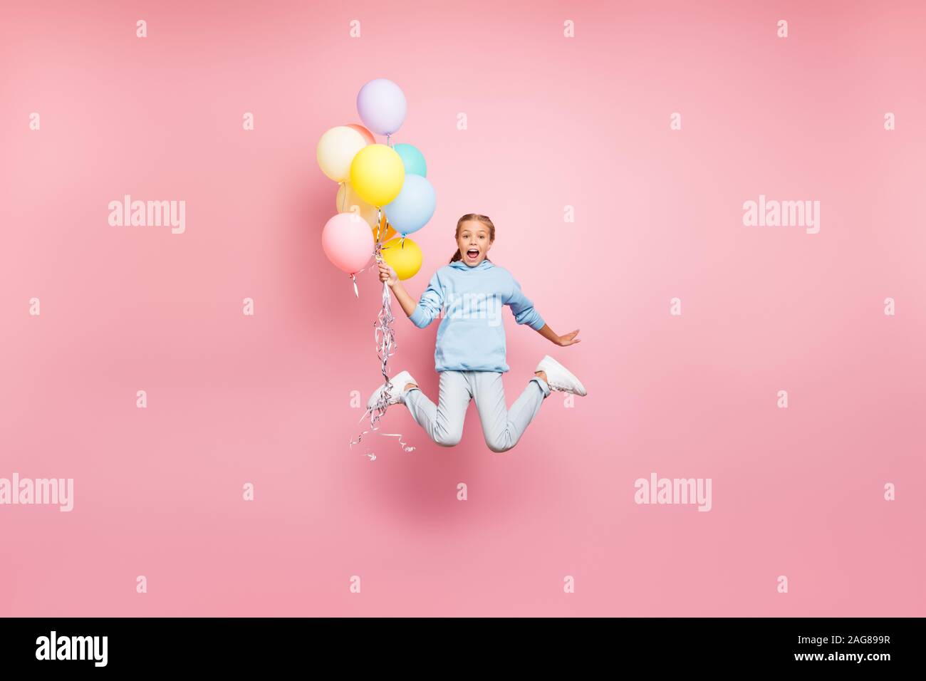 Full length body size photo of cheerfu positive cute nice screaming funny comic girl holding balloons with hands shouting flying jumping in blue Stock Photo