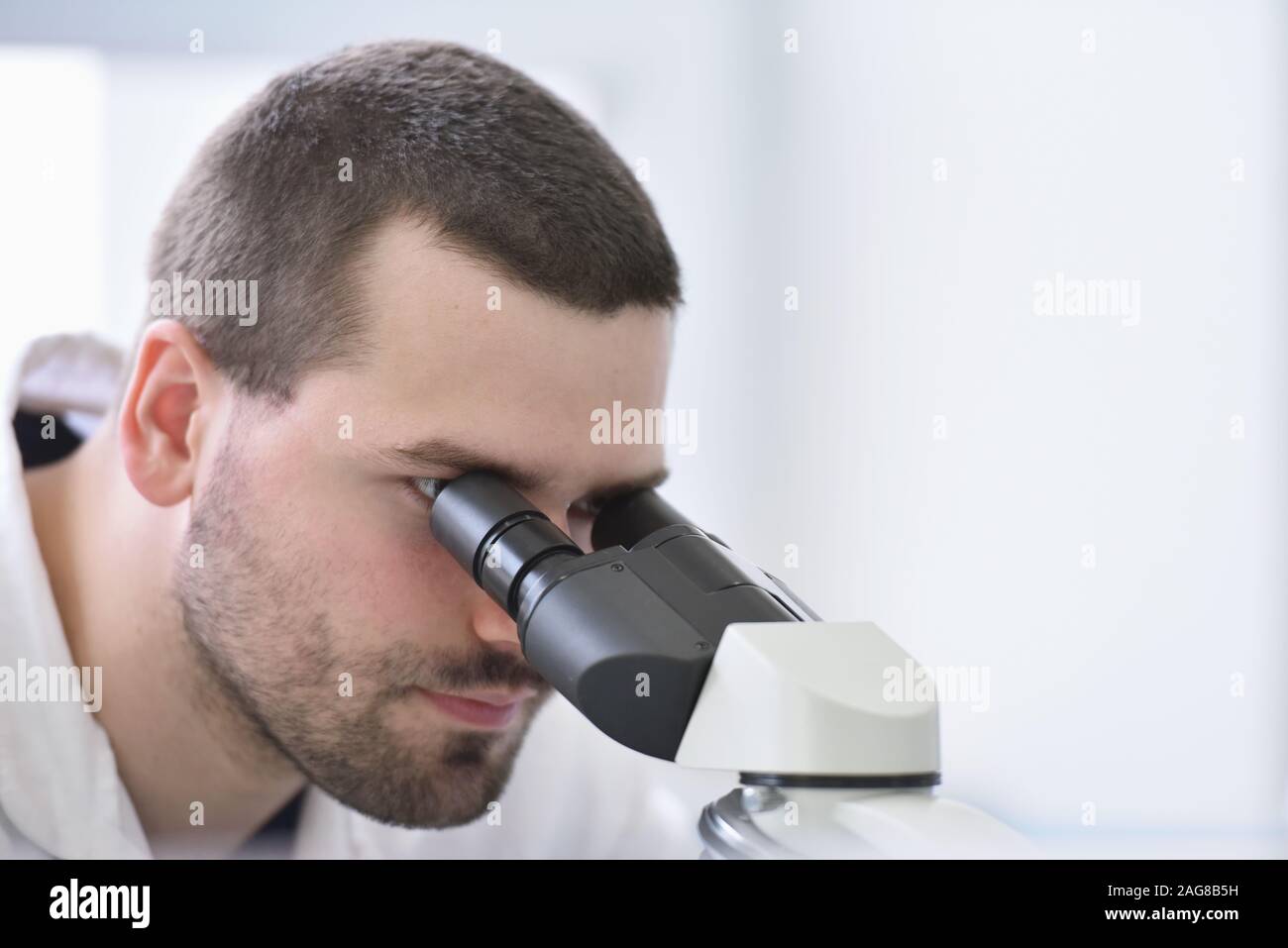 Young male scientist looking through a microscope in a laboratory doing ...