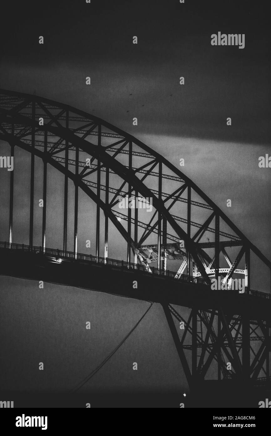 Vertical grayscale shot of a modern iron  arch-shaped bridge Stock Photo