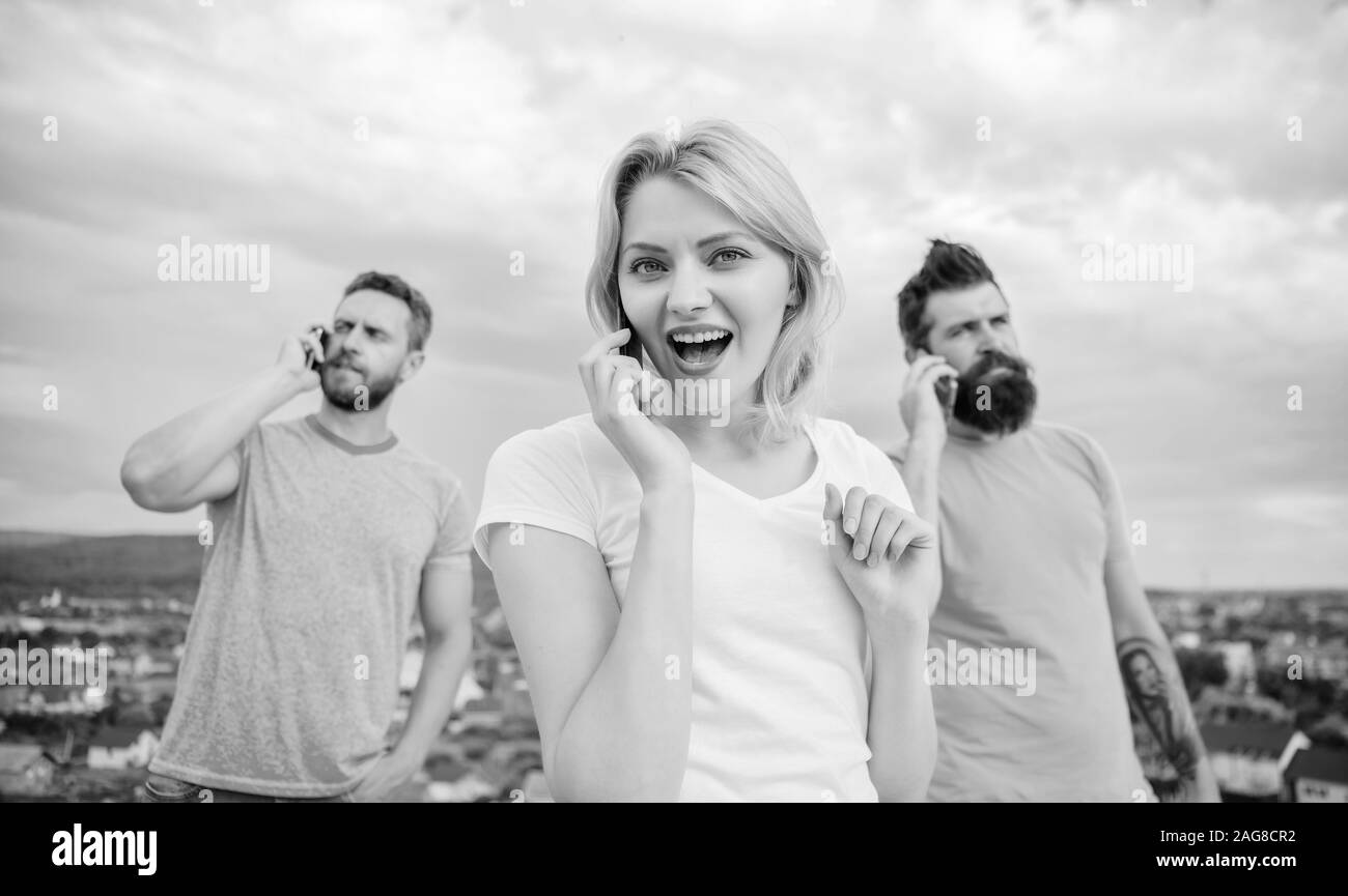 Beautiful young woman talking on the mobile phone and smiling near standing friends chatting in the sky background. Stock Photo