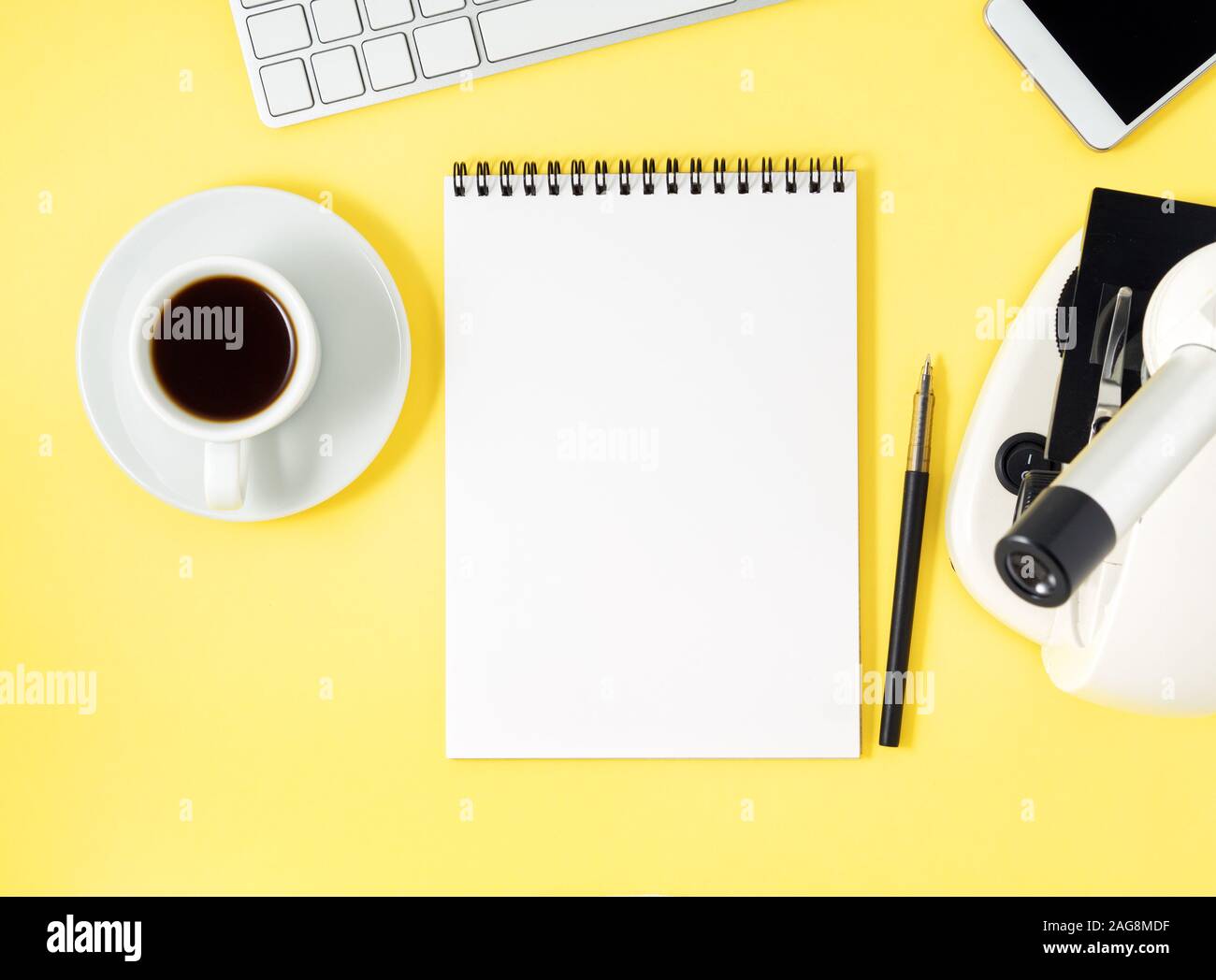Top view of a yellow office desktop with microscope, notepad, computer