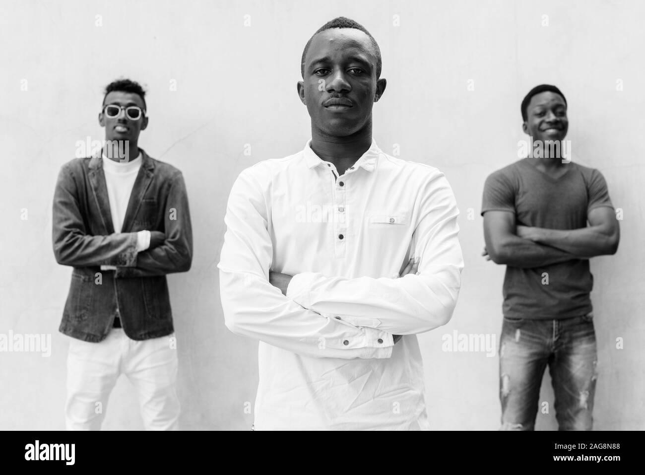 Three young African men hanging out against concrete wall outdoors Stock Photo