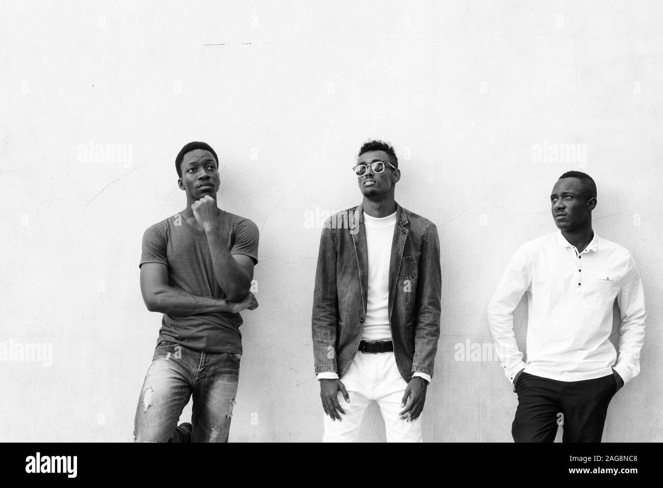 Three young African men hanging out against concrete wall outdoors Stock Photo