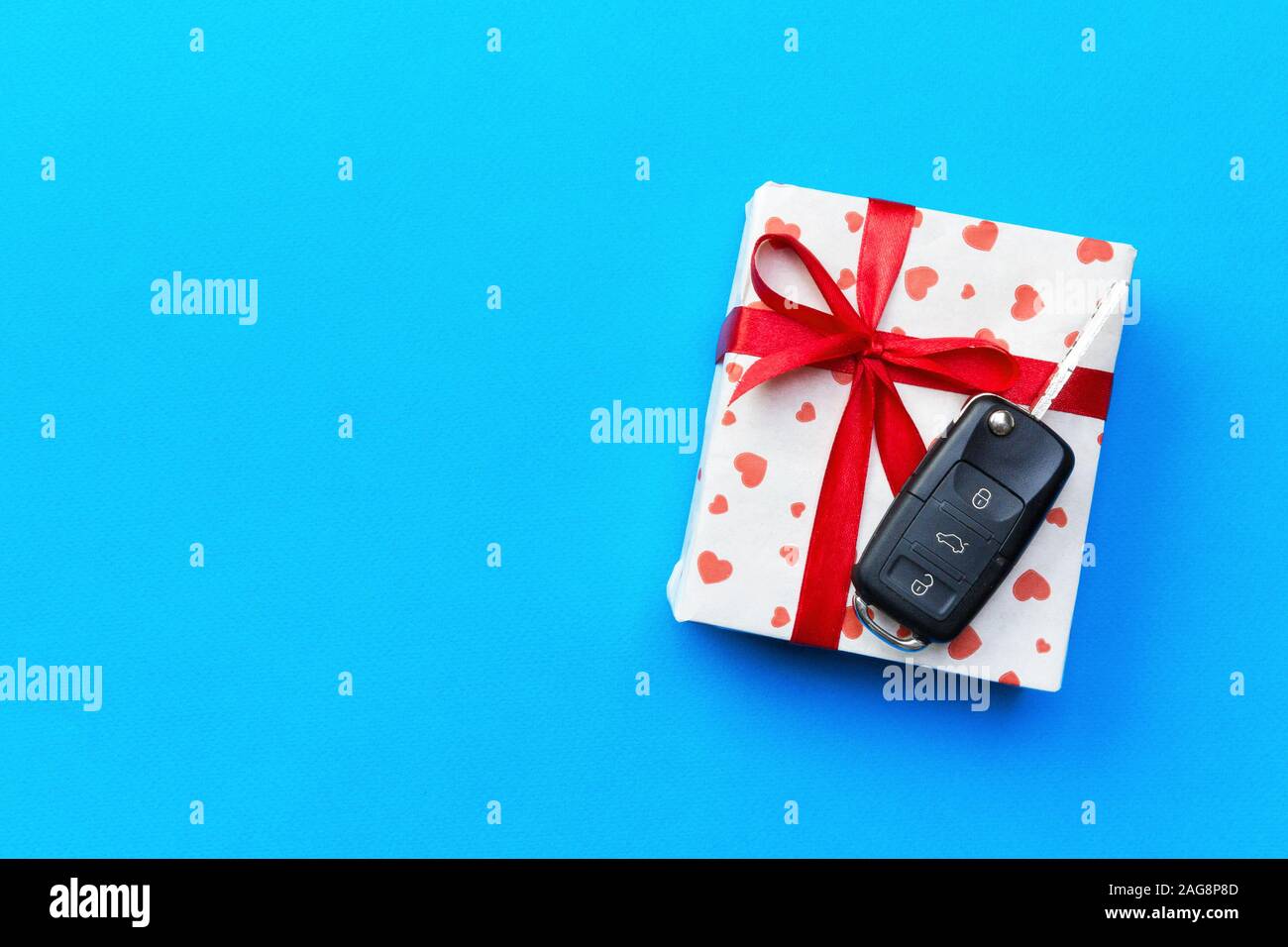 Car key on paper gift box with red ribbon bow and heart on blue table ...