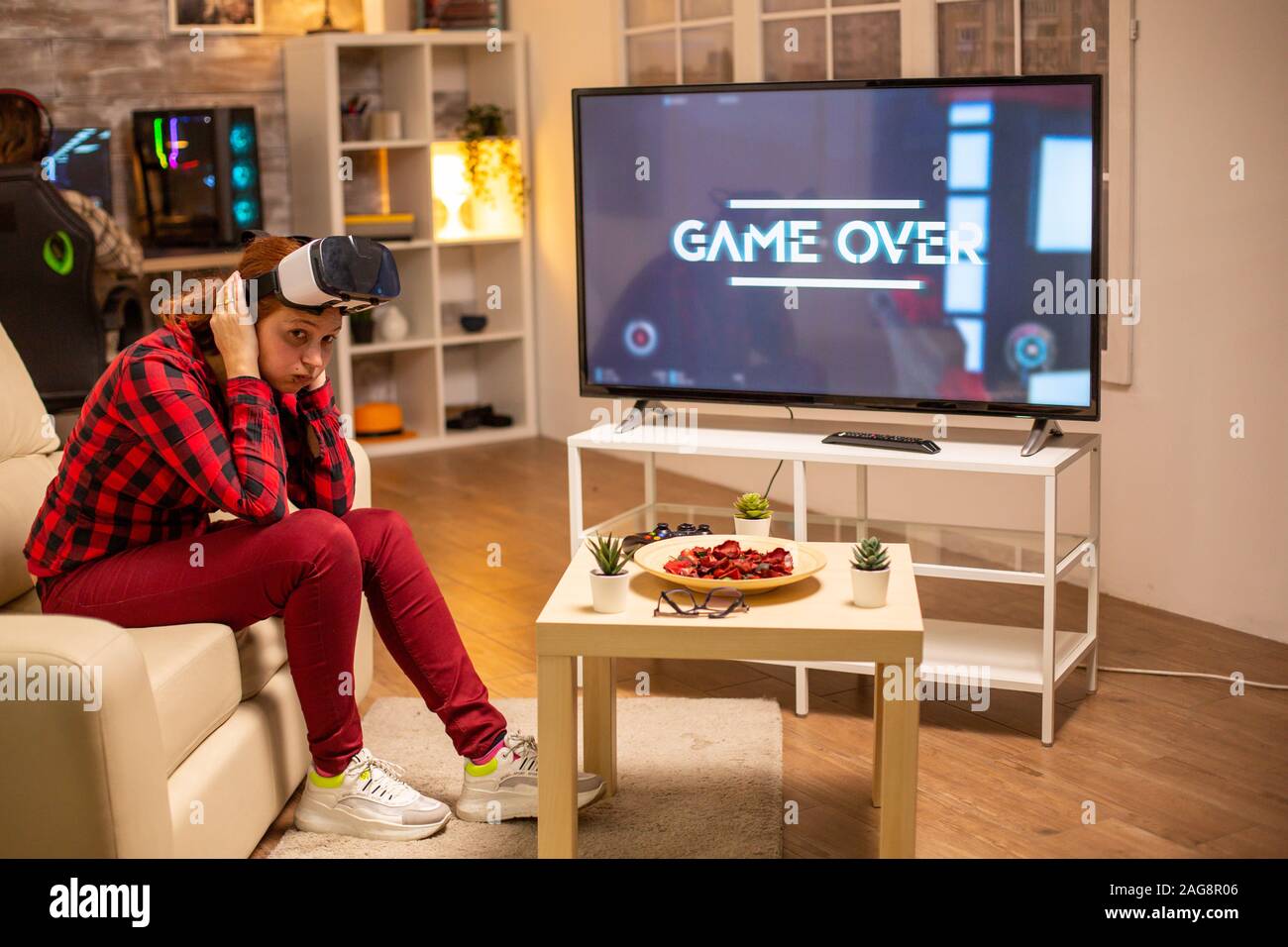 Woman losing at video games while playing using virtual reality headset late at night in the living room Stock Photo