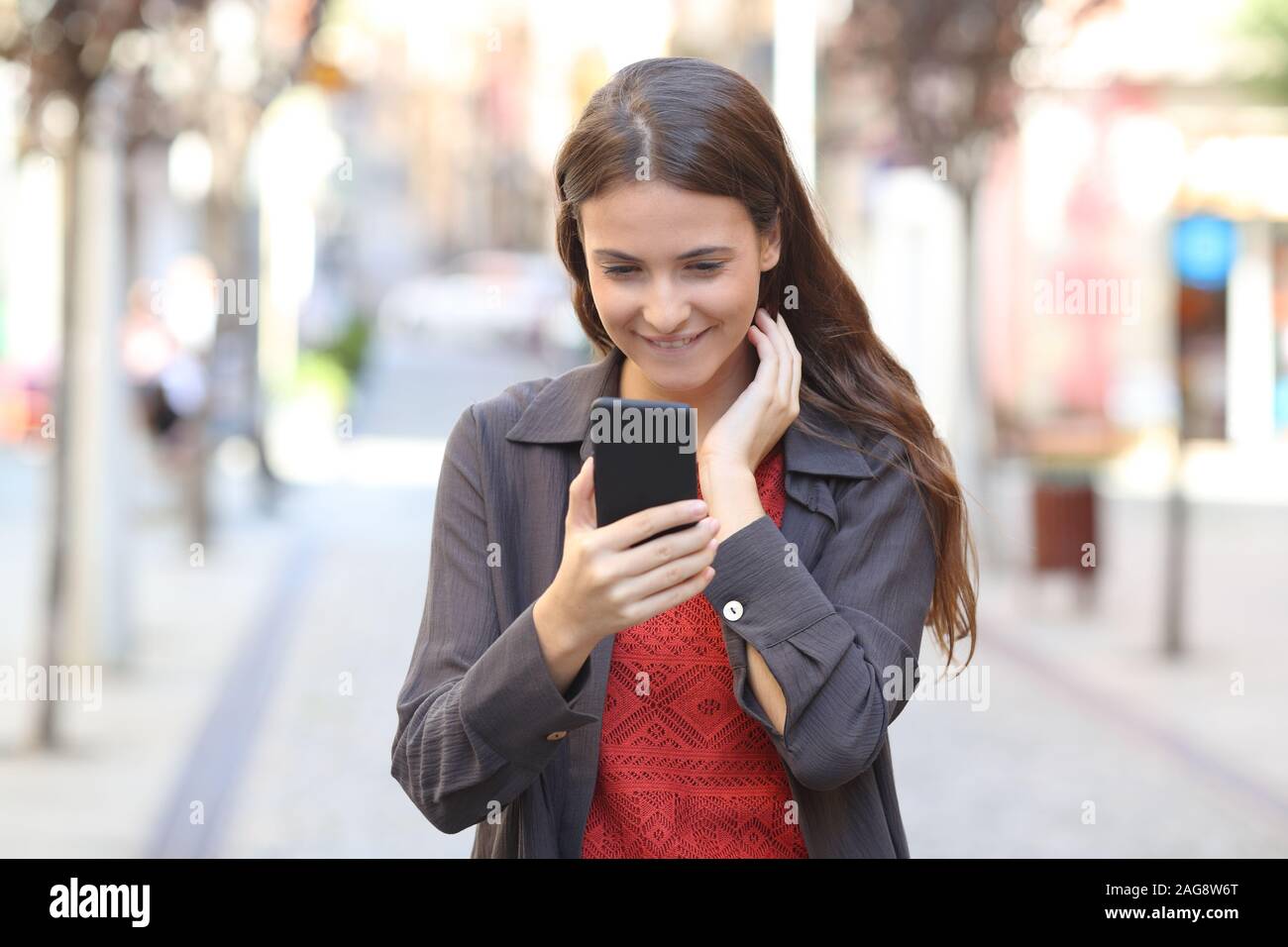 Front view portrait of a candid teen checking smart phone text walking in the street Stock Photo