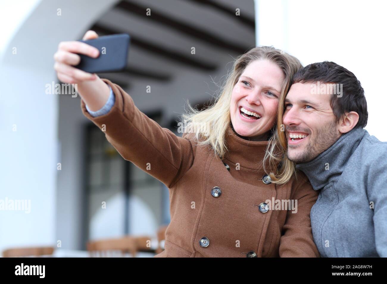 Happy couple of adults taking selfies with a mobile phone in winter in the street Stock Photo