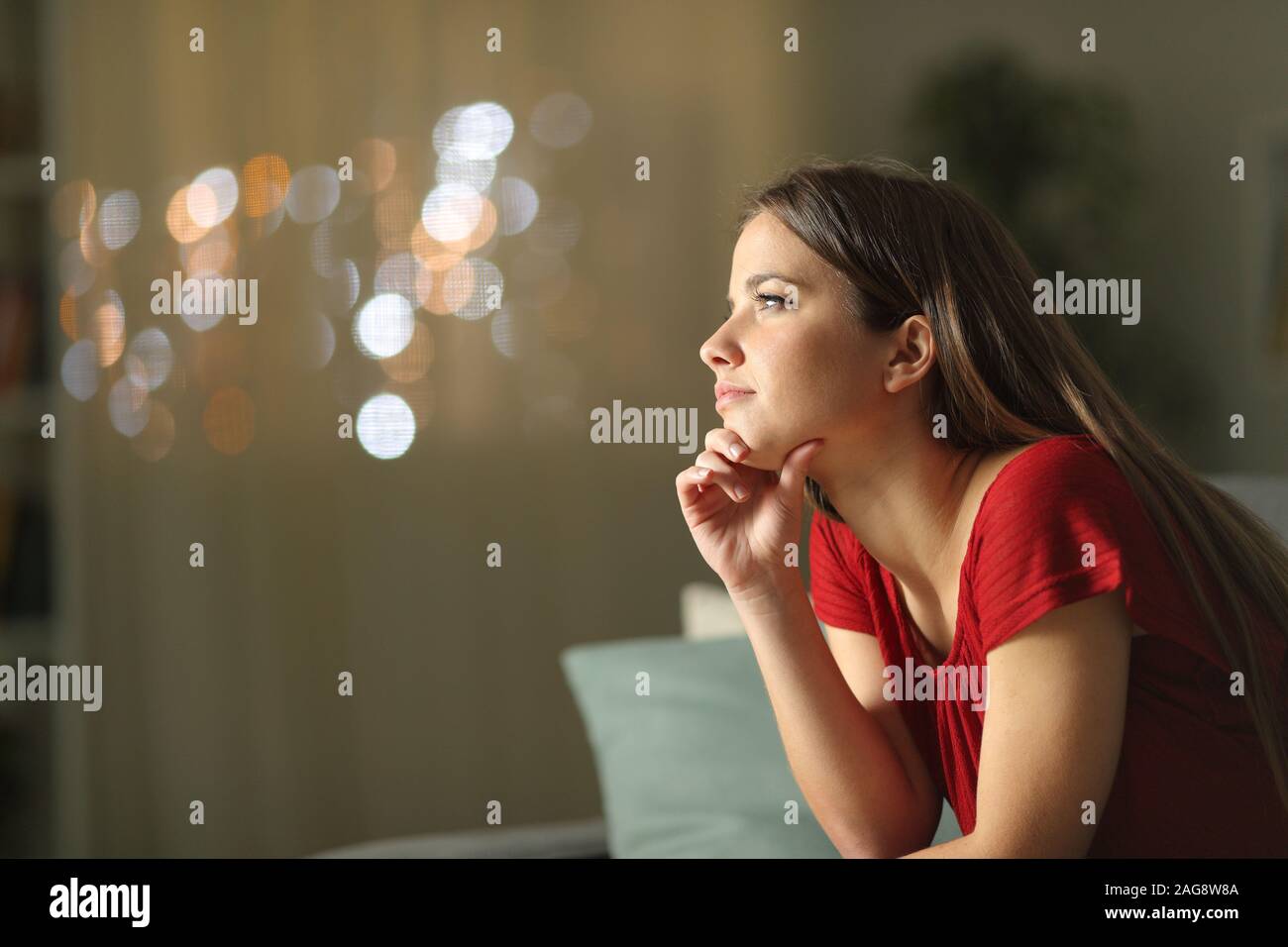Profile of a pensive woman looking away sitting on a couch in the night at home Stock Photo