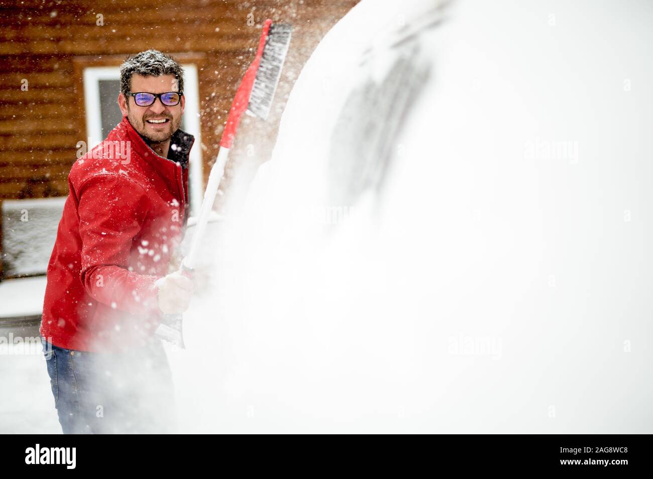 Male wearing a red winter jacket and cleaning snow off the car's window Stock Photo