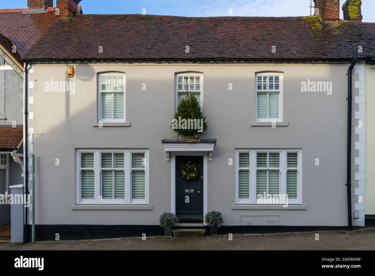 The exterior of an English home at Christmas with a wreath hanging from the front door and a Christmas on the porch roof Stock Photo