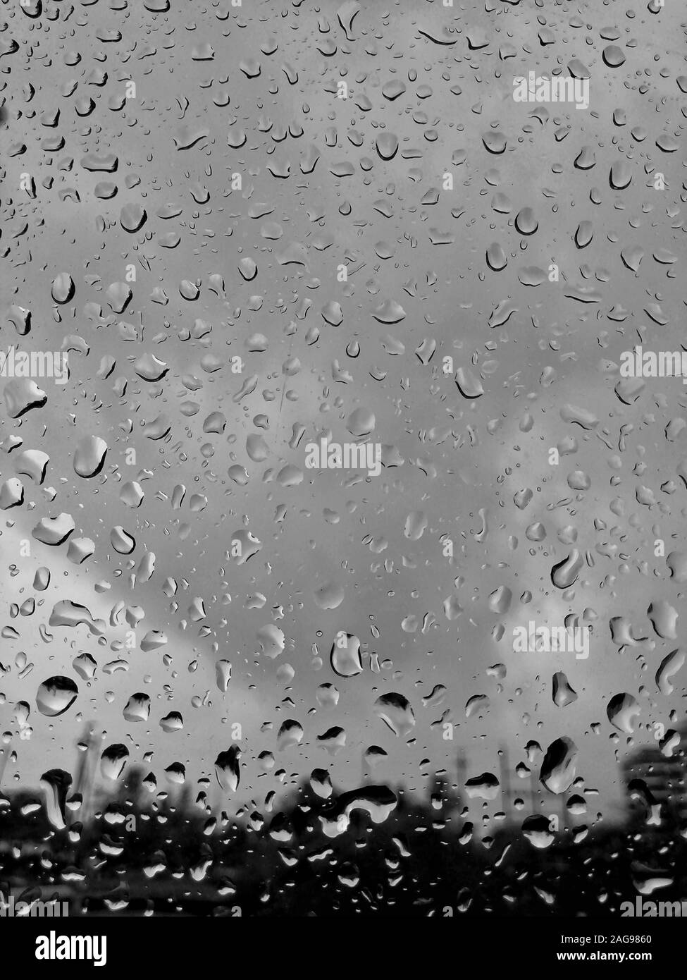 Vertical grayscale shot of raindrops on the glass during gloomy weather ...