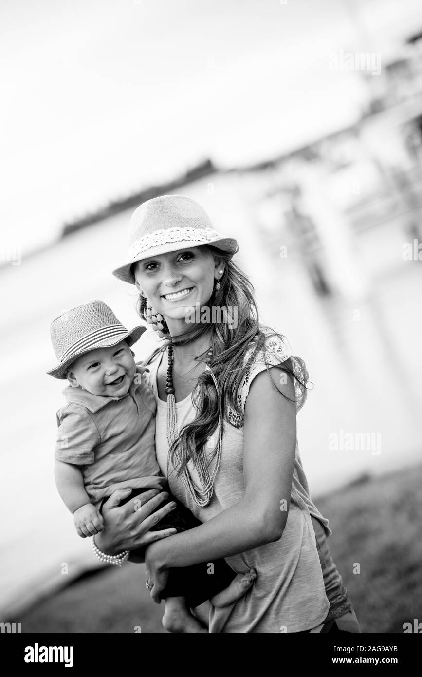 Vertical grayscale shot of a mother holding her child while smiling at the camera Stock Photo