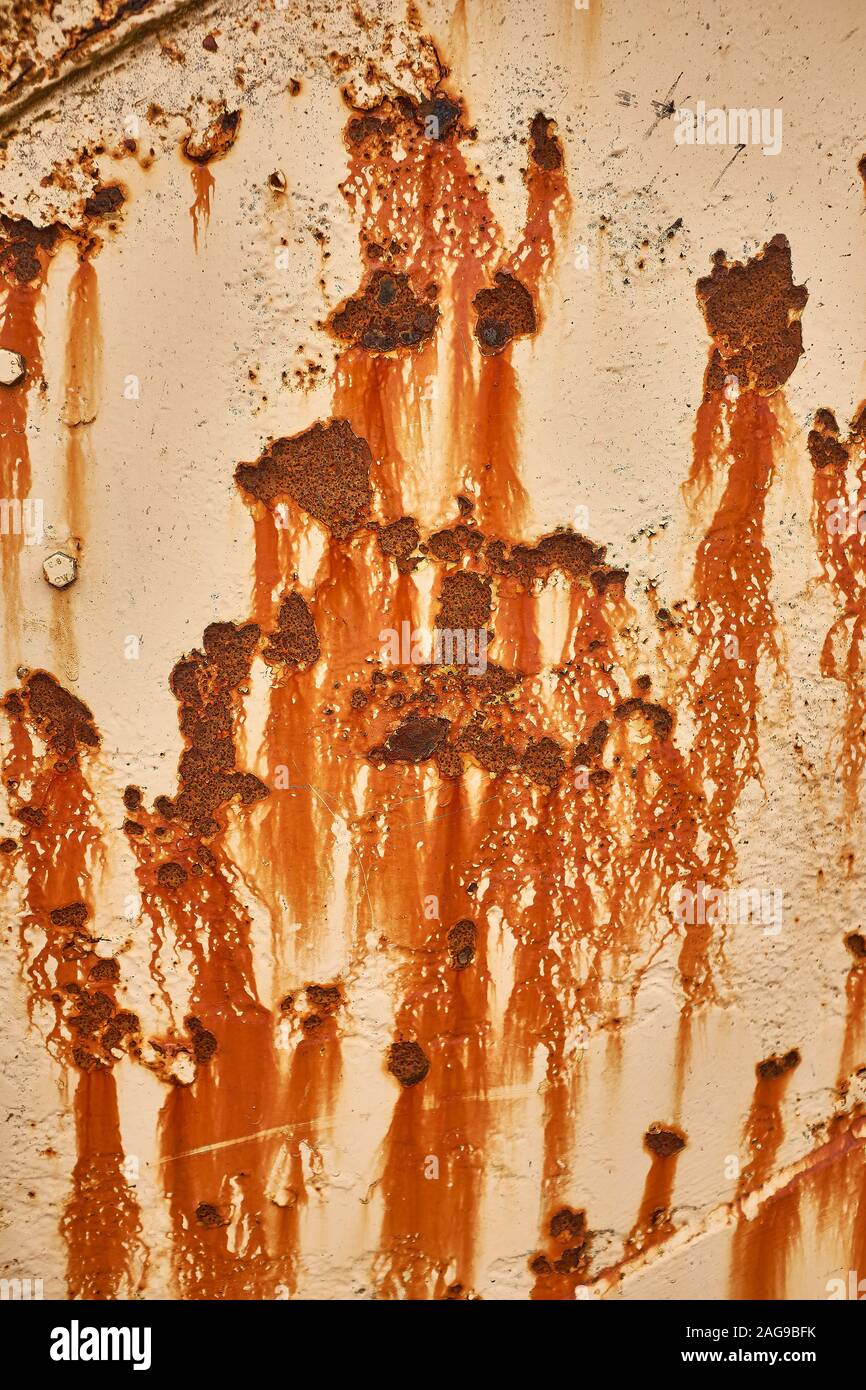 A close up of an old piece of metal that has been rusting for a long time with rust stains marking the cream paint Stock Photo