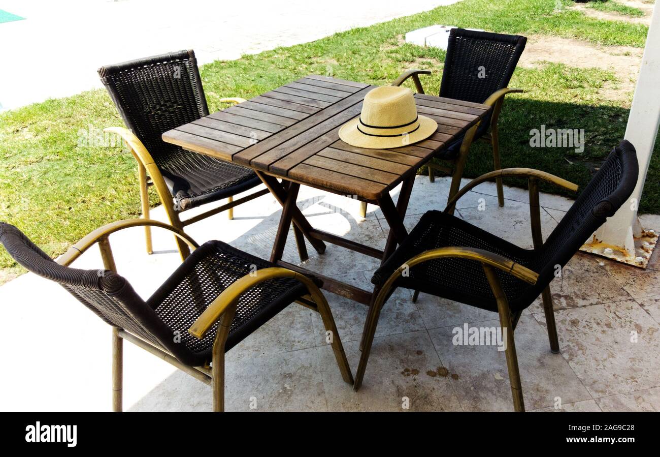 Top view of a straw hat left on a restaurant table with empty chairs around in outdoor setting at noon time. Stock Photo