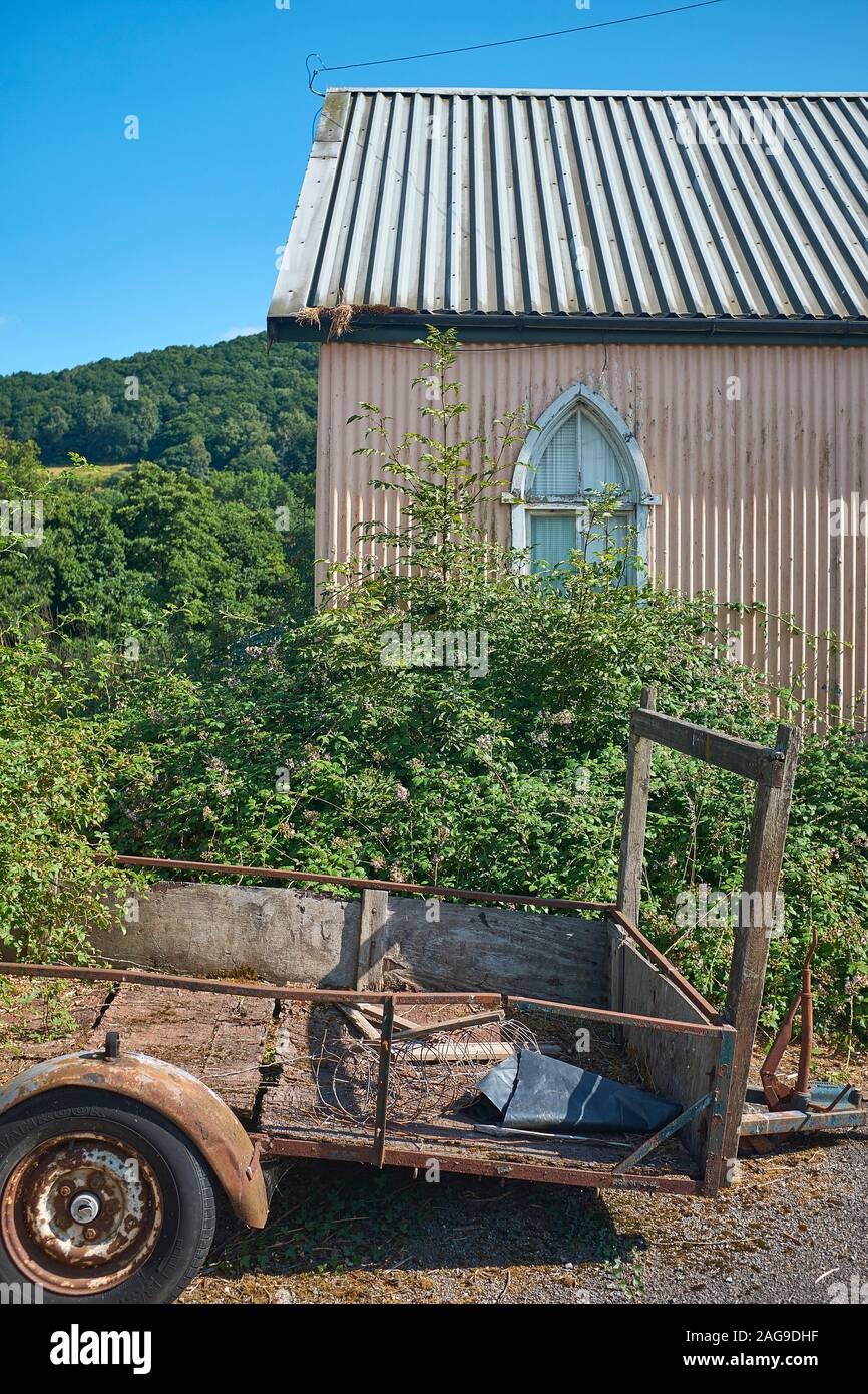 An old building that has been made from corrugated sheeting that has an arched window and an old worn out trailer outside, Talybont- on- Usk, Wales Stock Photo