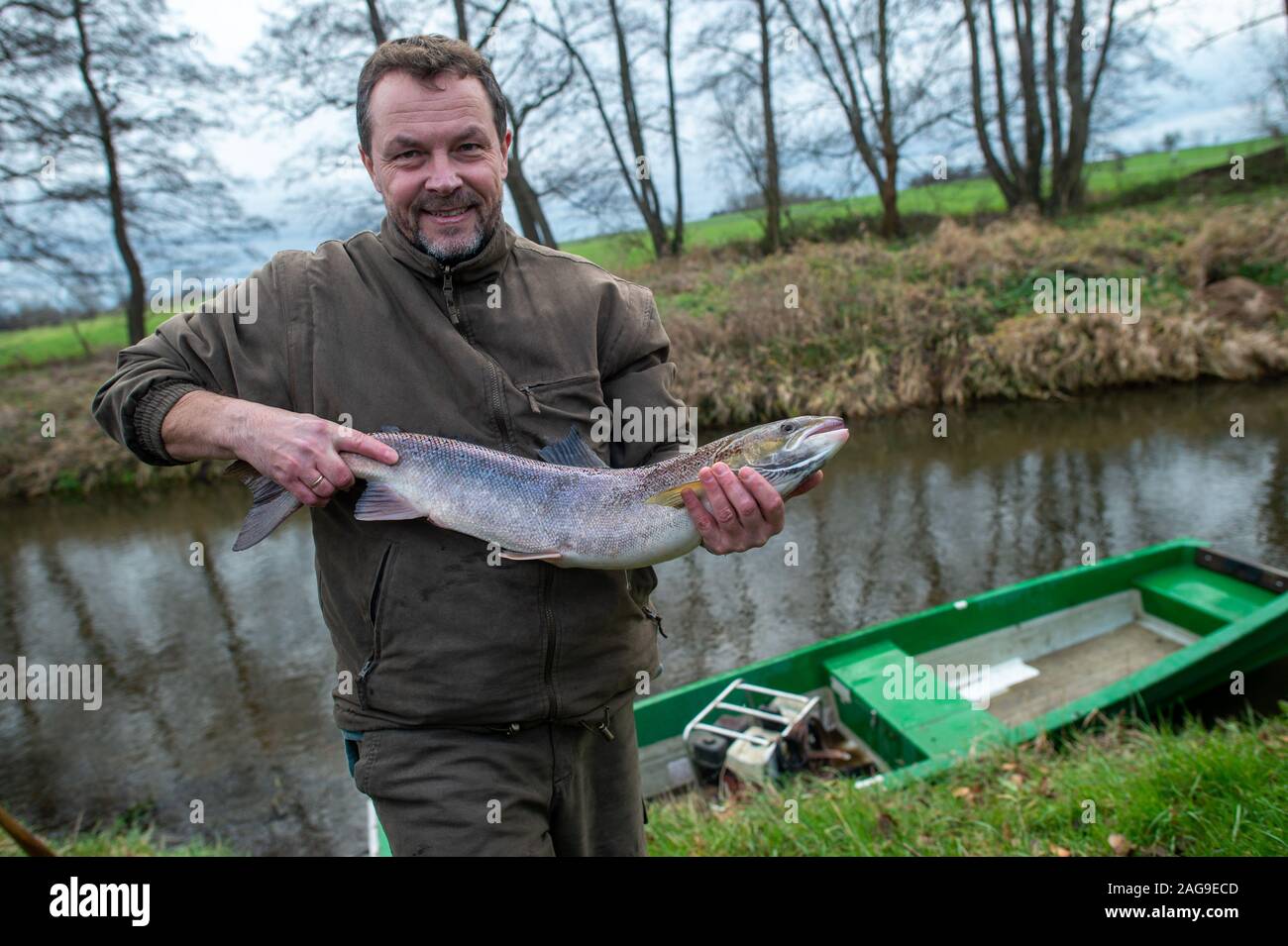 18 December 2019, Saxony-Anhalt, Nutha: Steffen Zahn, project manager of the Migratory Fish Programme Saxony-Anhalt of the Institute for Inland Fisheries in Potsdam, holds a 4 kilo female salmon in his hands on the Nuthe. The fish had been caught during the trial fishing on the Nuthe. There the animal was released 3 to 4 years ago what the fishermen noticed at a mark on the pelvic fin. In the meantime, the salmon had swum as far as the Atlantic and has now returned to the Nuthe for spawning. In the Nuthe a total of 143500 young salmon and 90300 sea trout hatchlings have been released so far. P Stock Photo